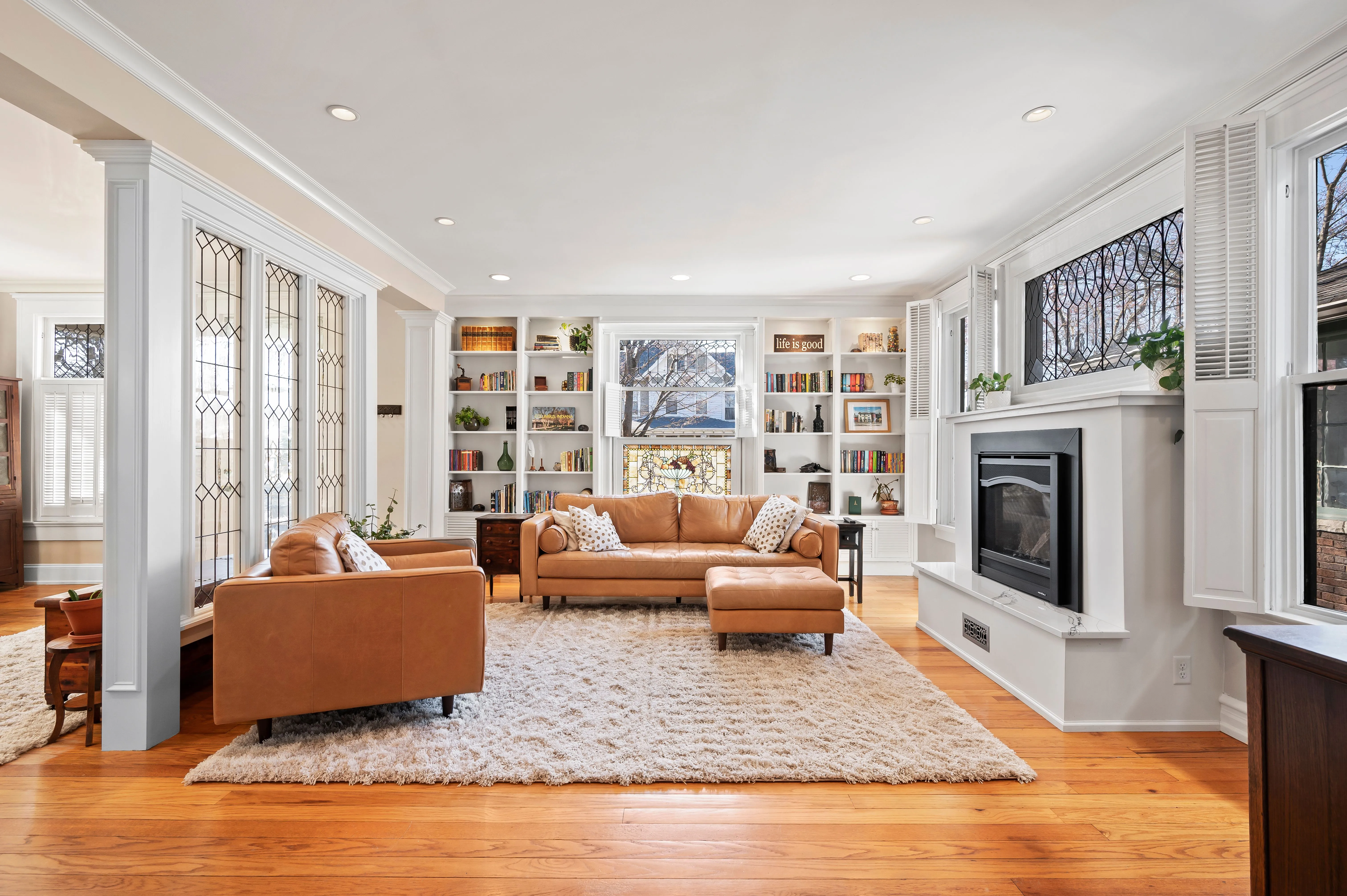 Elegant living room interior with hardwood floors, leather sofas, fireplace, and built-in shelving.