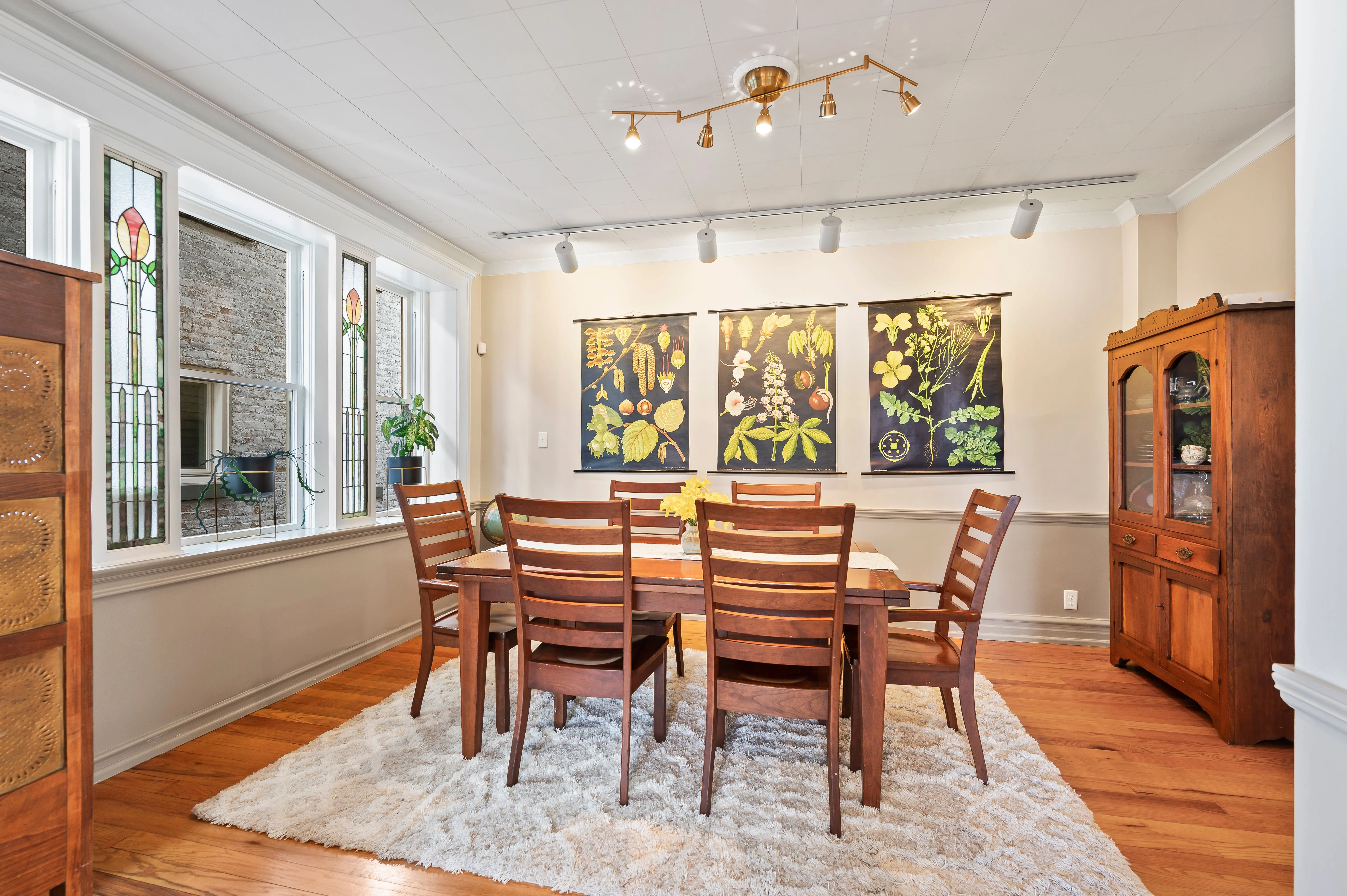 Bright dining room with wooden table and chairs, hardwood floors, white area rug, and artwork on the walls.