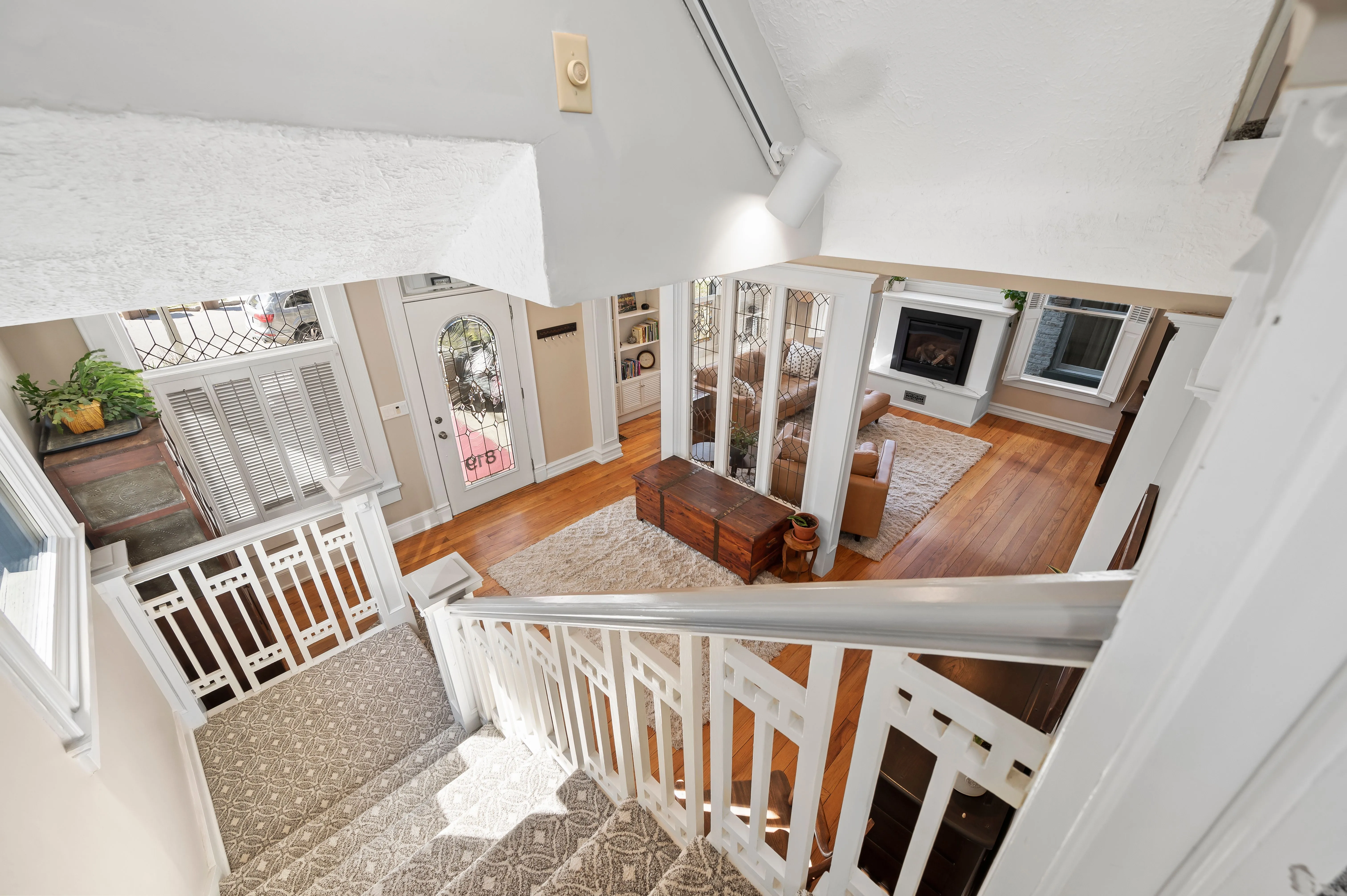 Overhead view of a multi-level home interior with white railing, wood flooring, and a glimpse into the living areas.