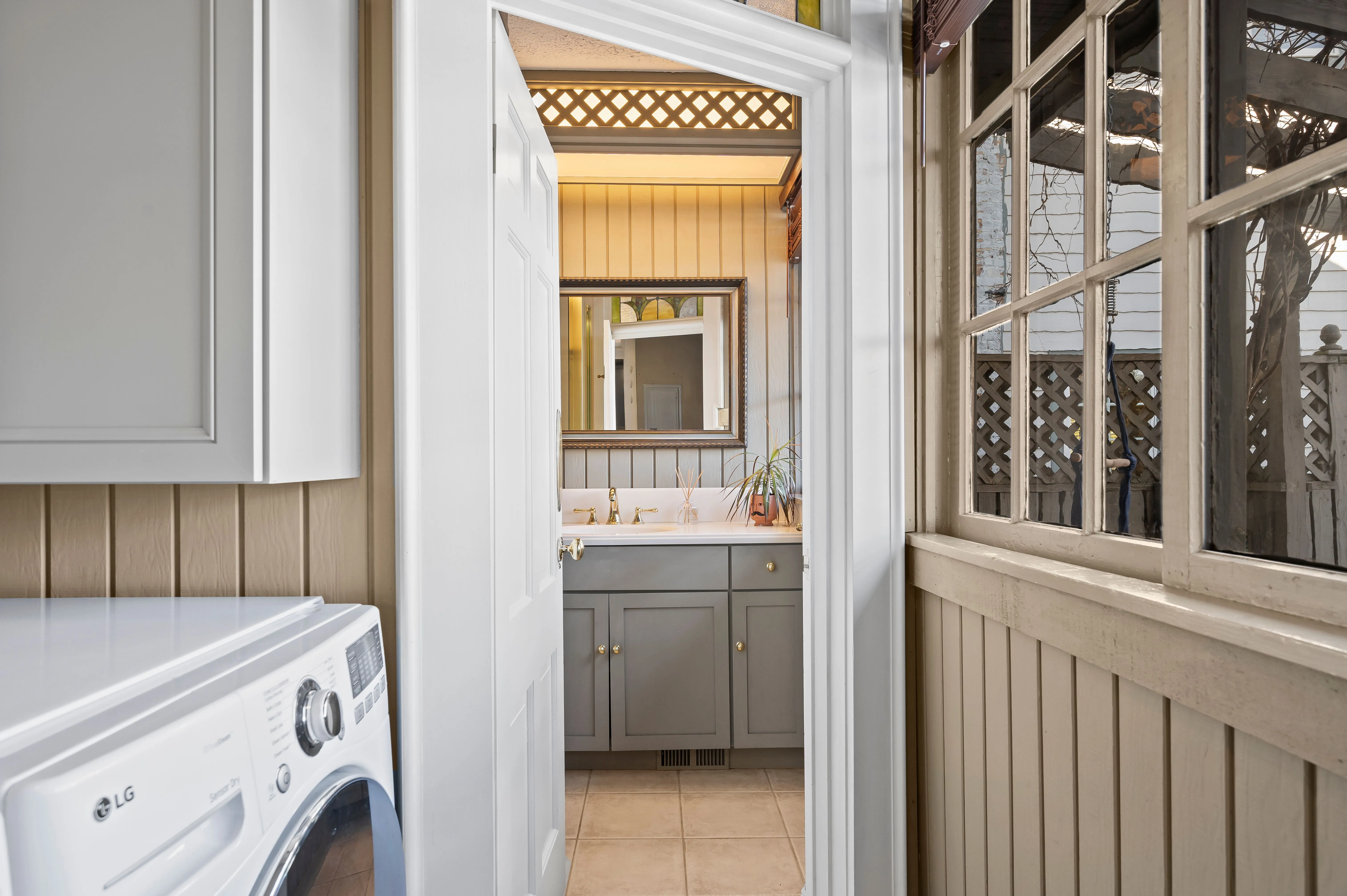 View from a laundry room with a white washing machine, through an open door leading to a well-lit kitchen.