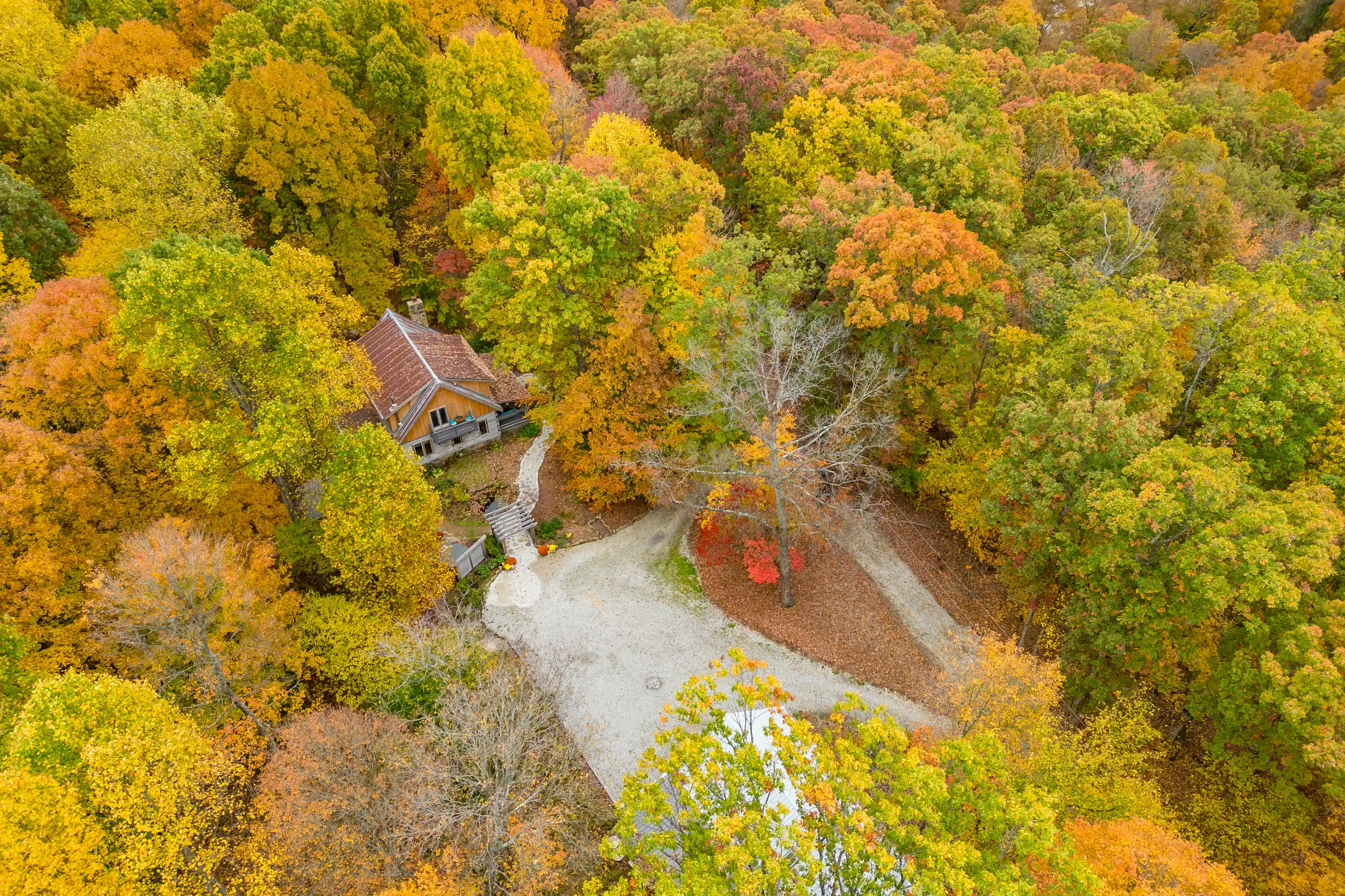 Aerial view of a house surrounded by a forest with colorful autumn foliage.