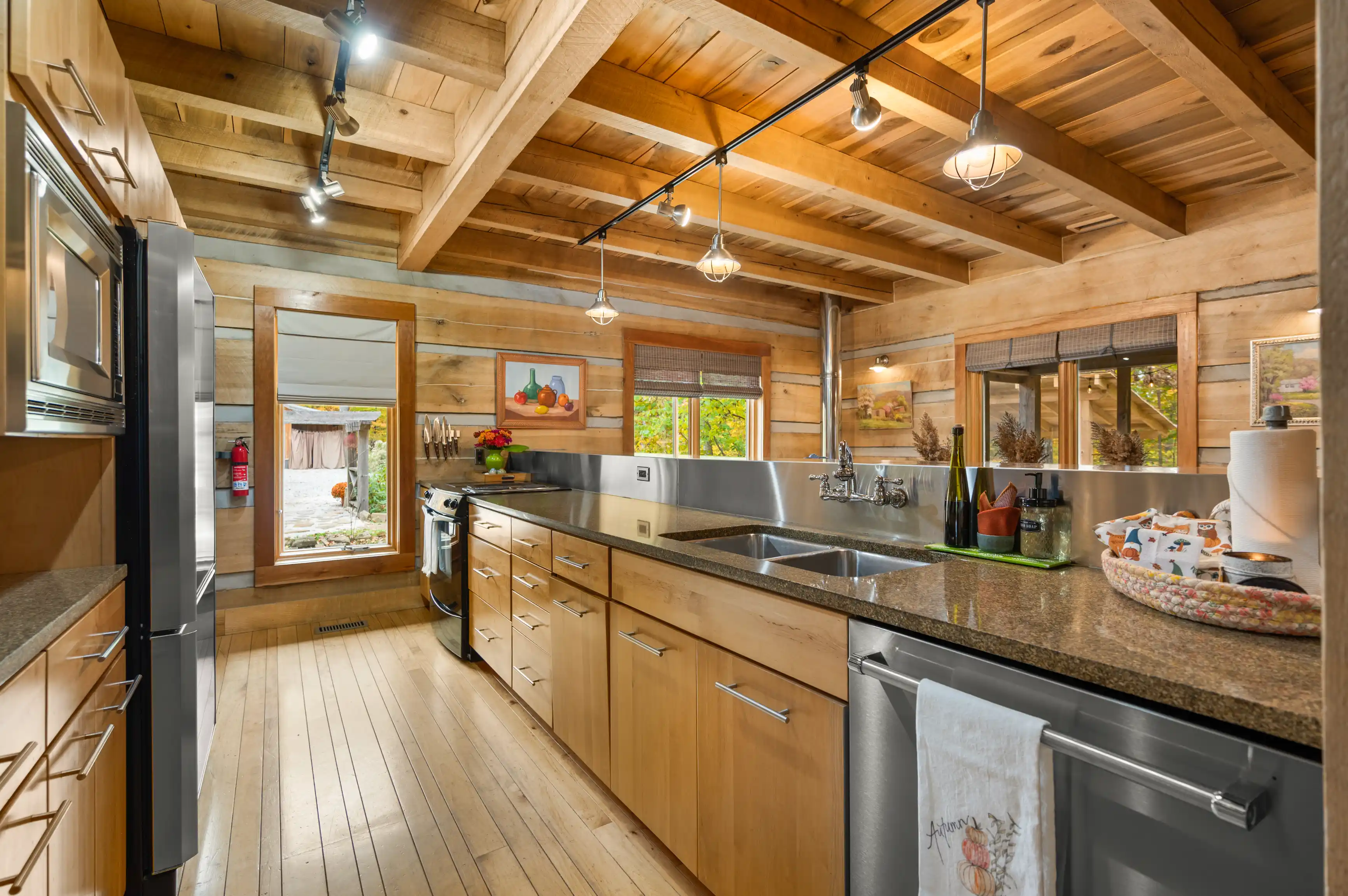 Spacious rustic kitchen interior with wooden beams, cabinetry, stainless steel appliances, and a granite countertop.