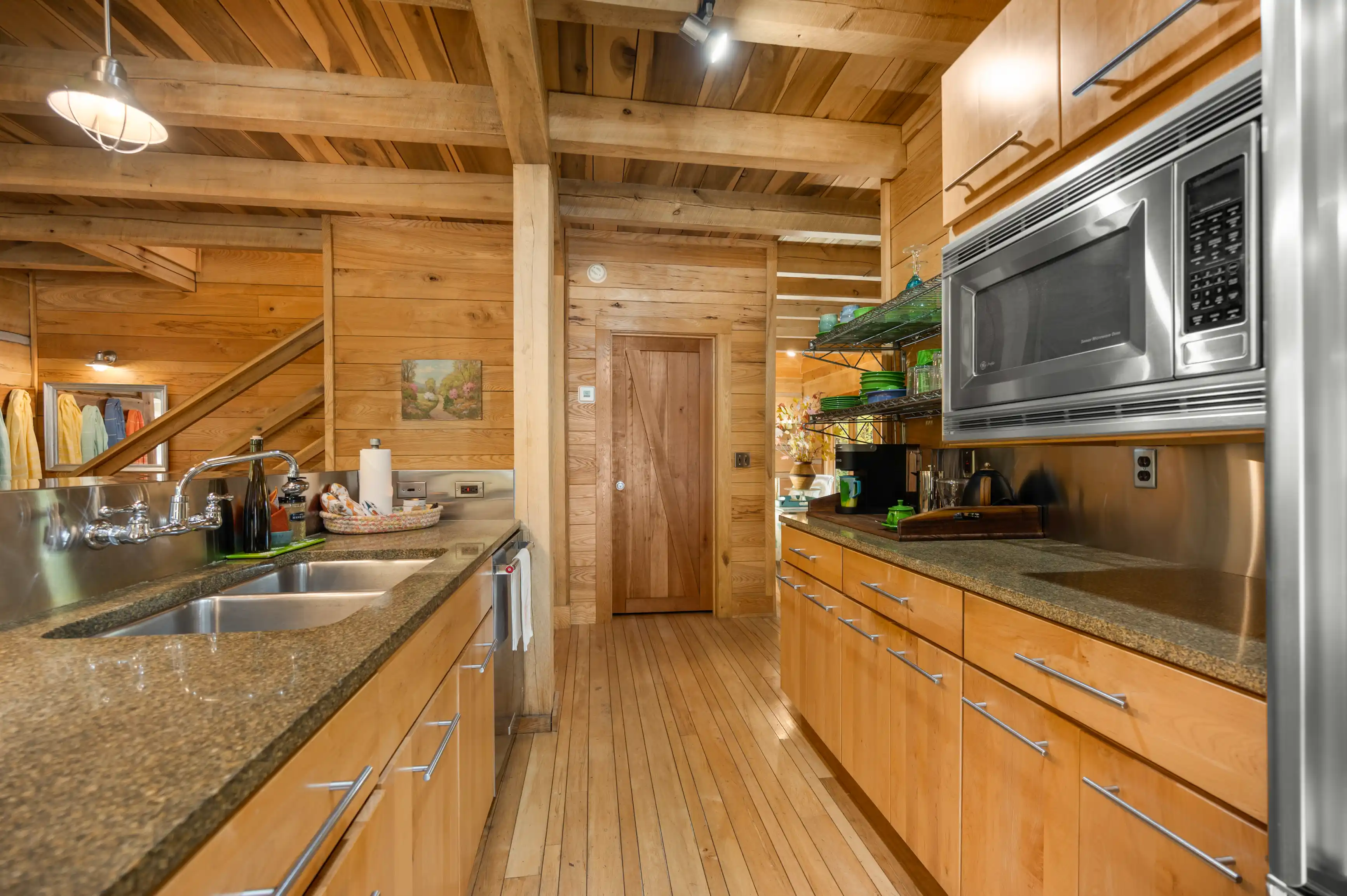 Interior of a cozy wooden cabin kitchen with stainless steel appliances, wooden cabinets, and granite countertops.