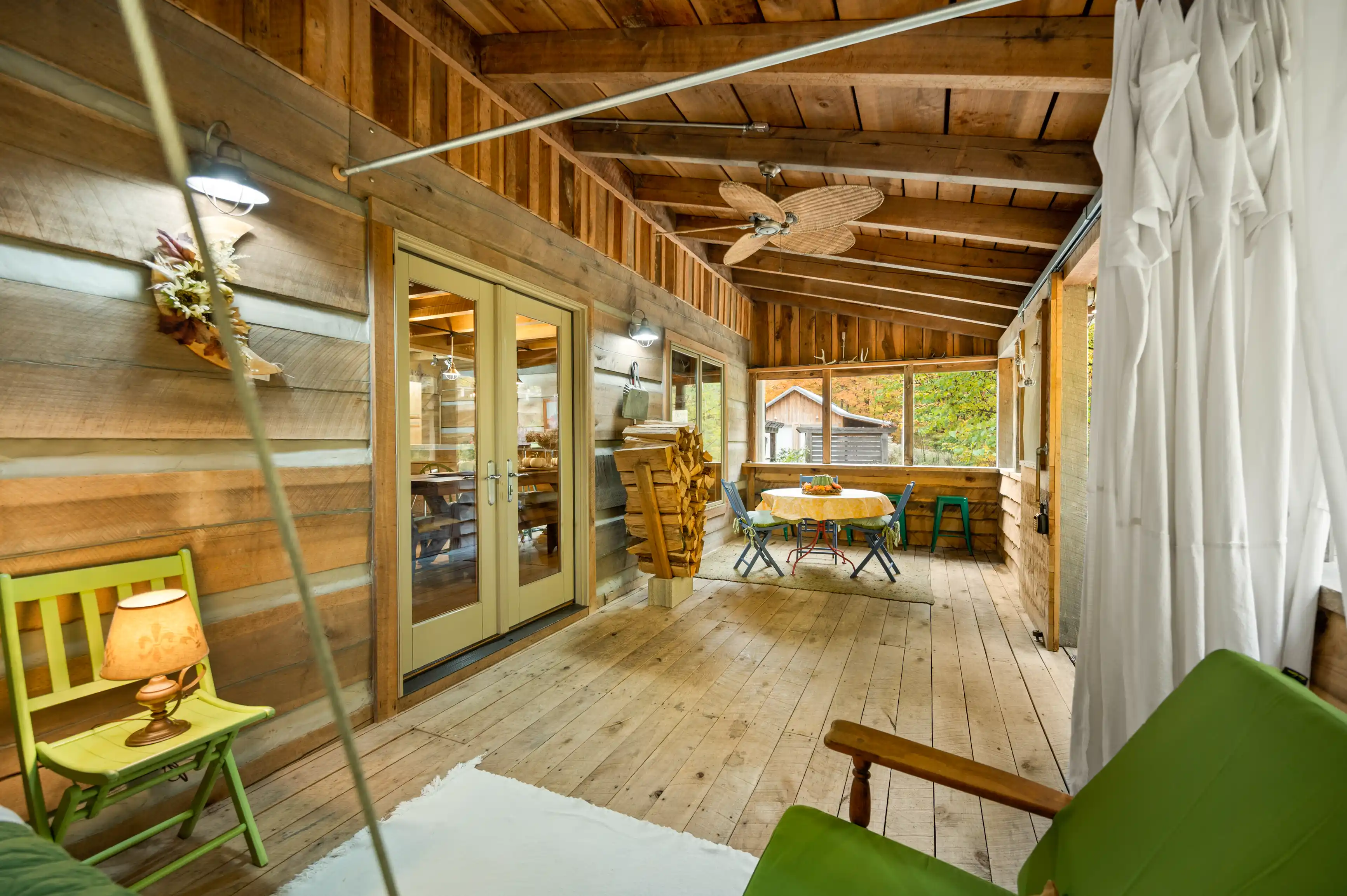 Cozy screened porch with wooden furnishings, ceiling fan, and glass door leading to the interior of a rustic cabin.