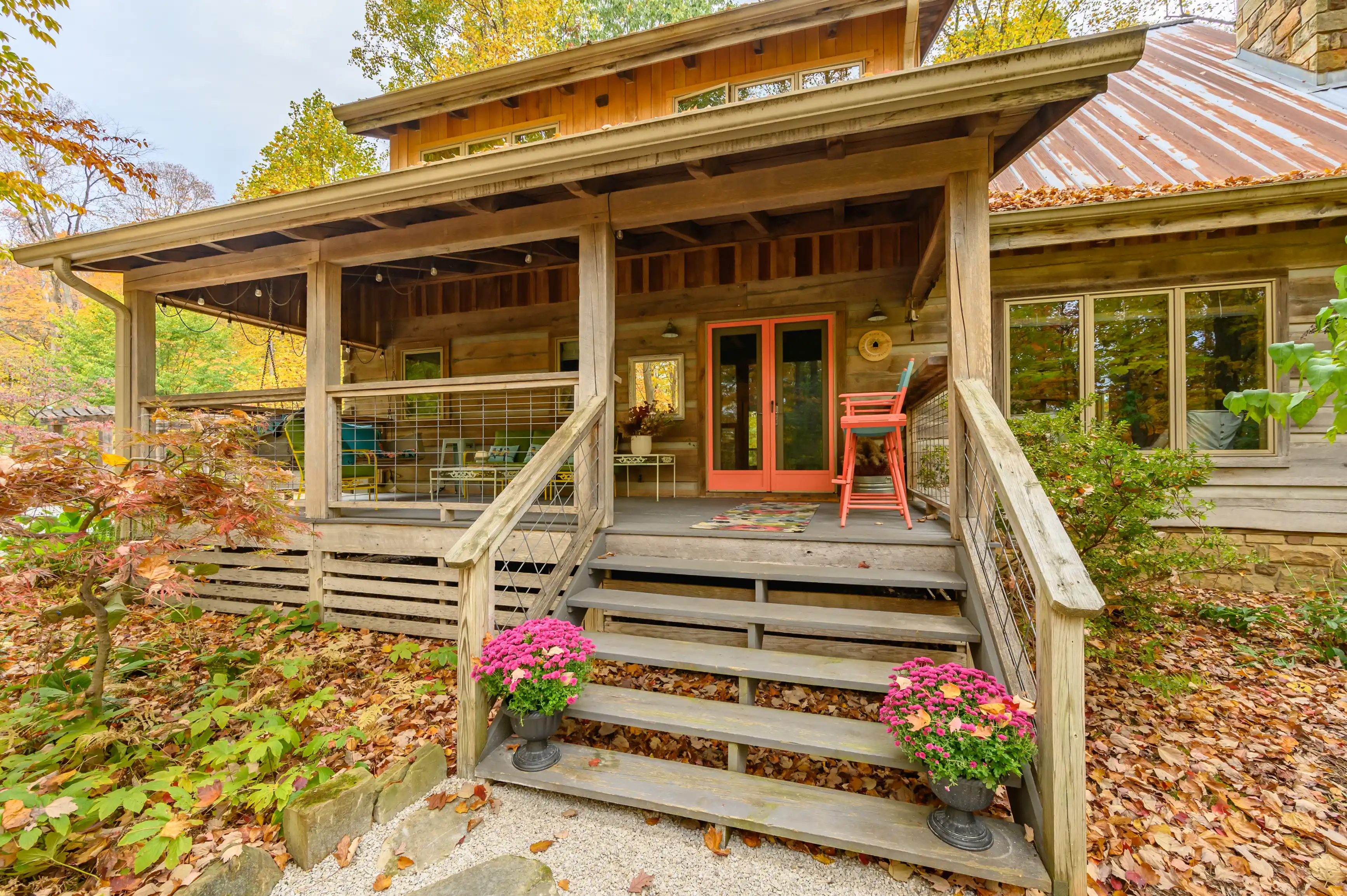 Rustic wooden cabin with a covered porch, red door, and autumn foliage.