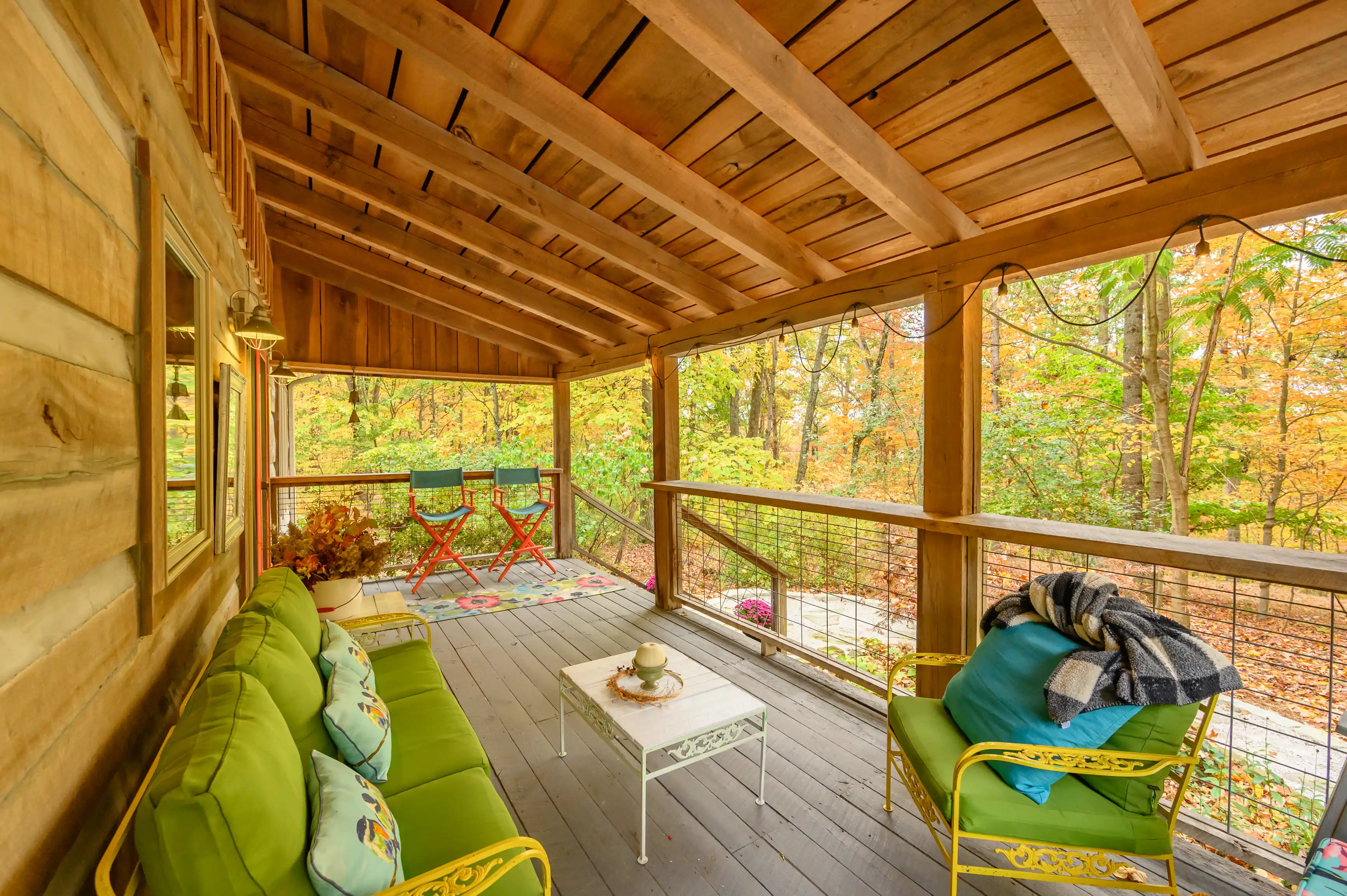 Cozy covered wooden porch with comfortable seating and autumn forest view.