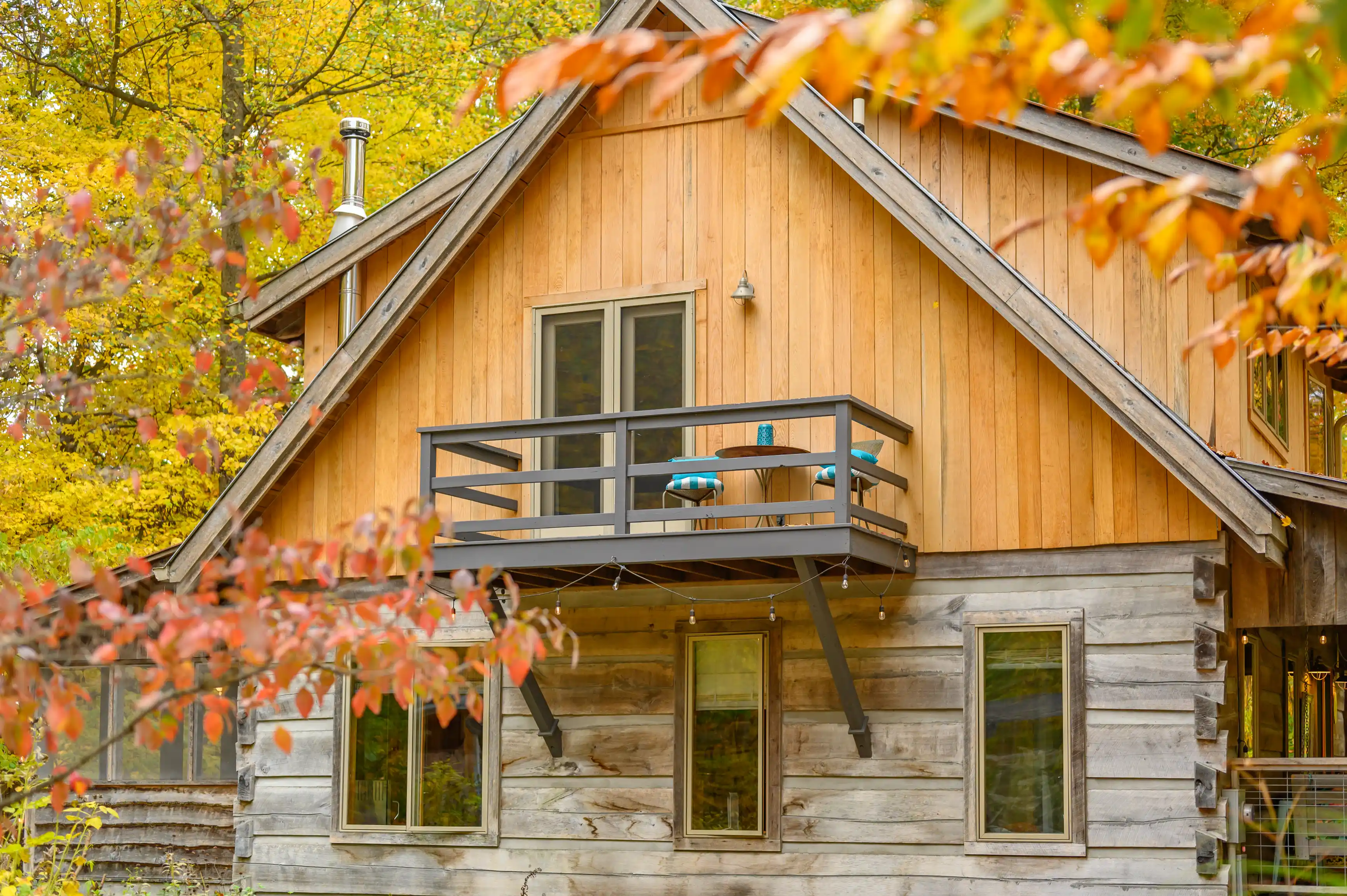 Wooden cabin with a balcony surrounded by autumn foliage, featuring a blue yoga mat.