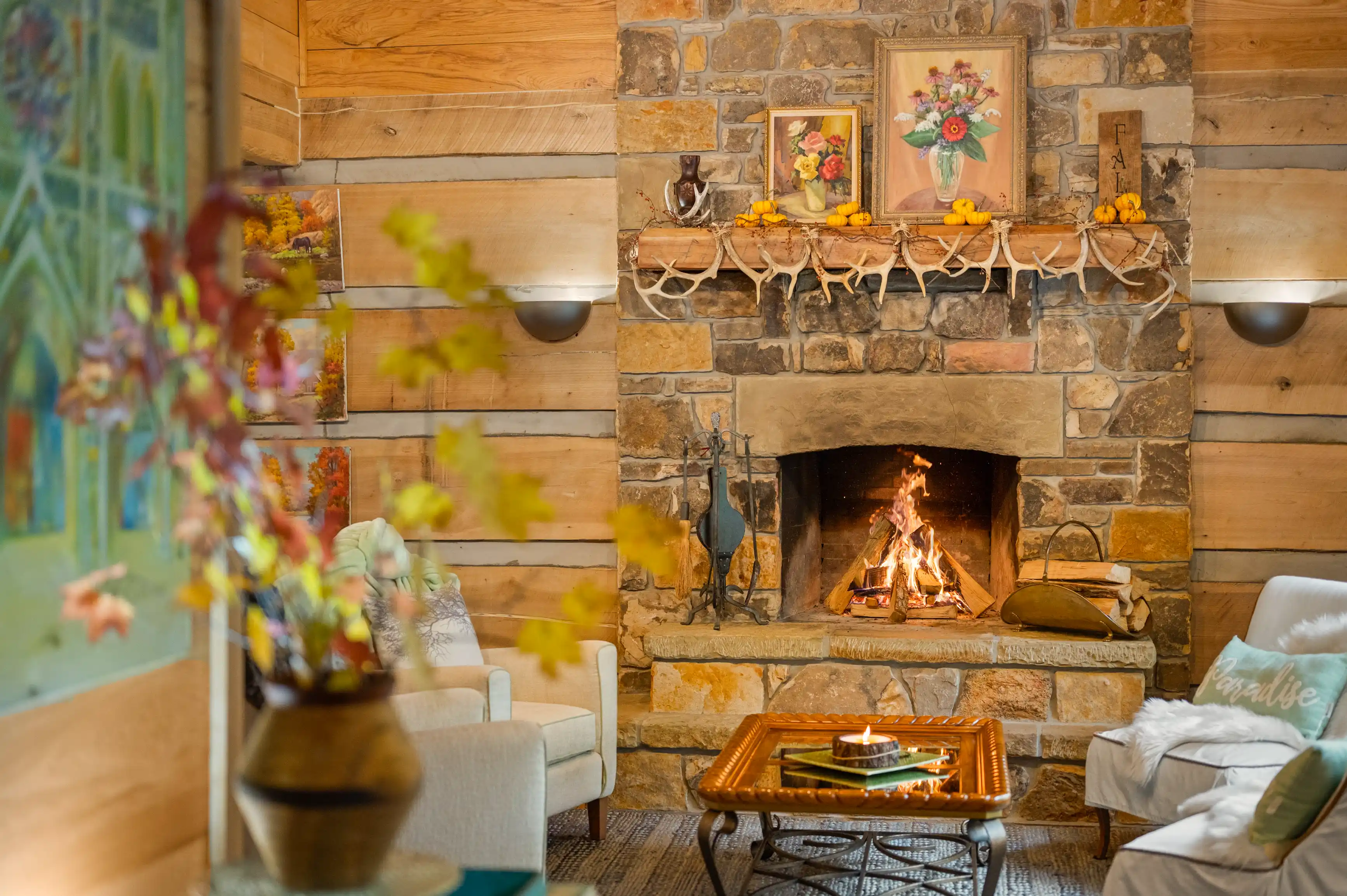 Cozy rustic living room interior with a lit fireplace, decorative mantle, wooden walls, and comfortable seating.