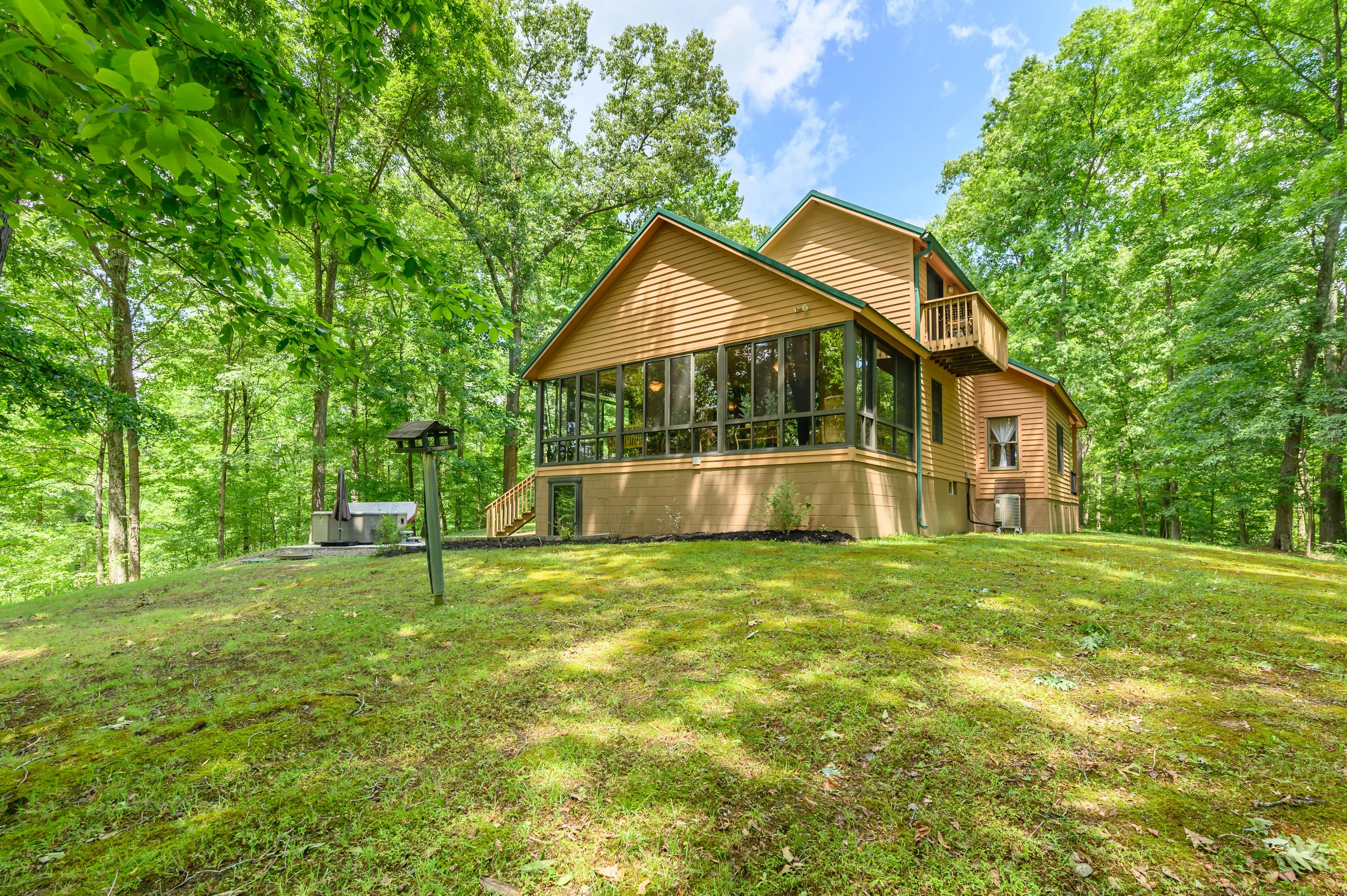 Wooden house with a screened-in porch surrounded by trees on a sunny day.