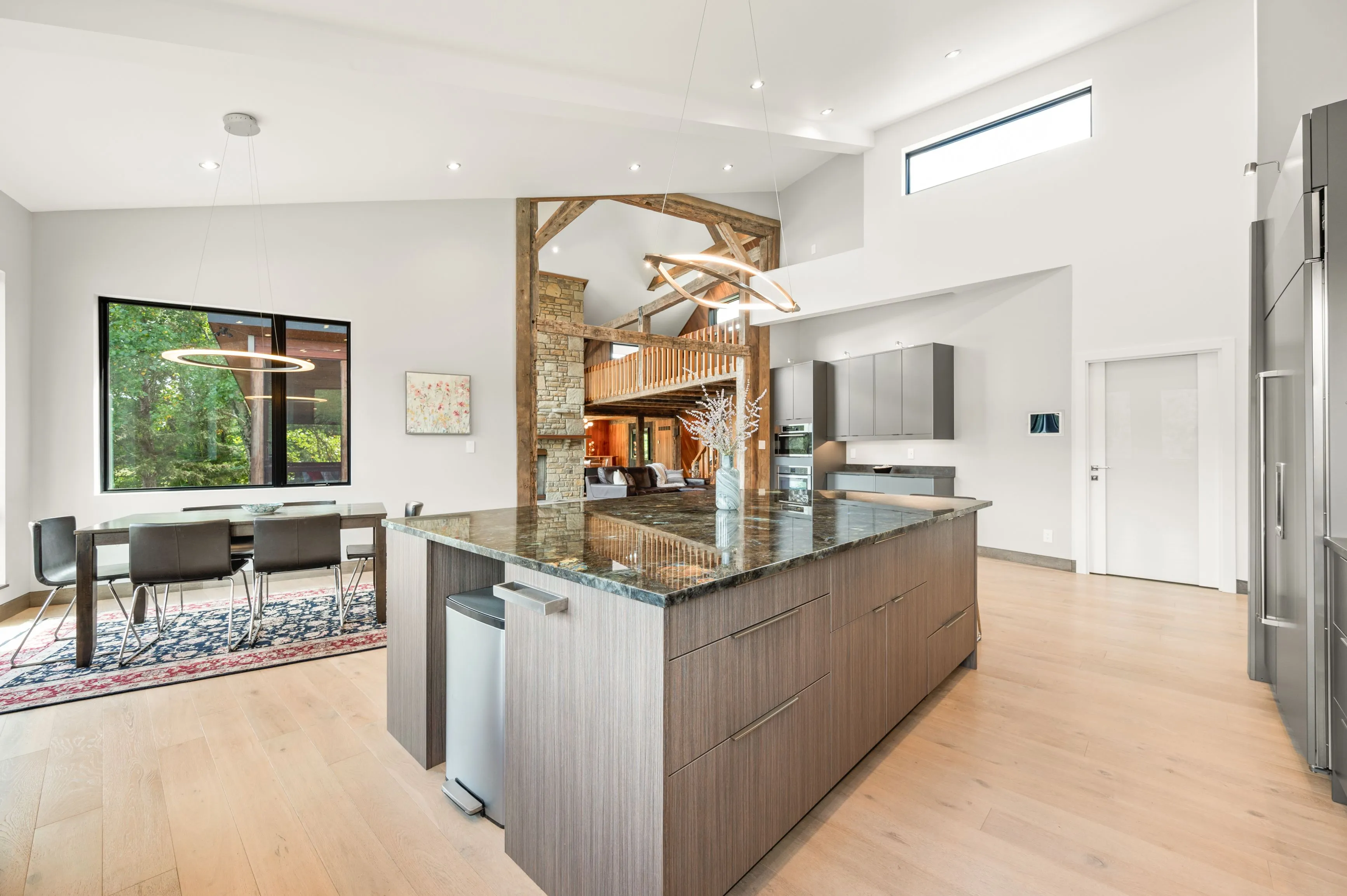 Modern kitchen interior with granite countertop island, stainless steel appliances, and an open-concept dining area with a large window overlooking greenery.