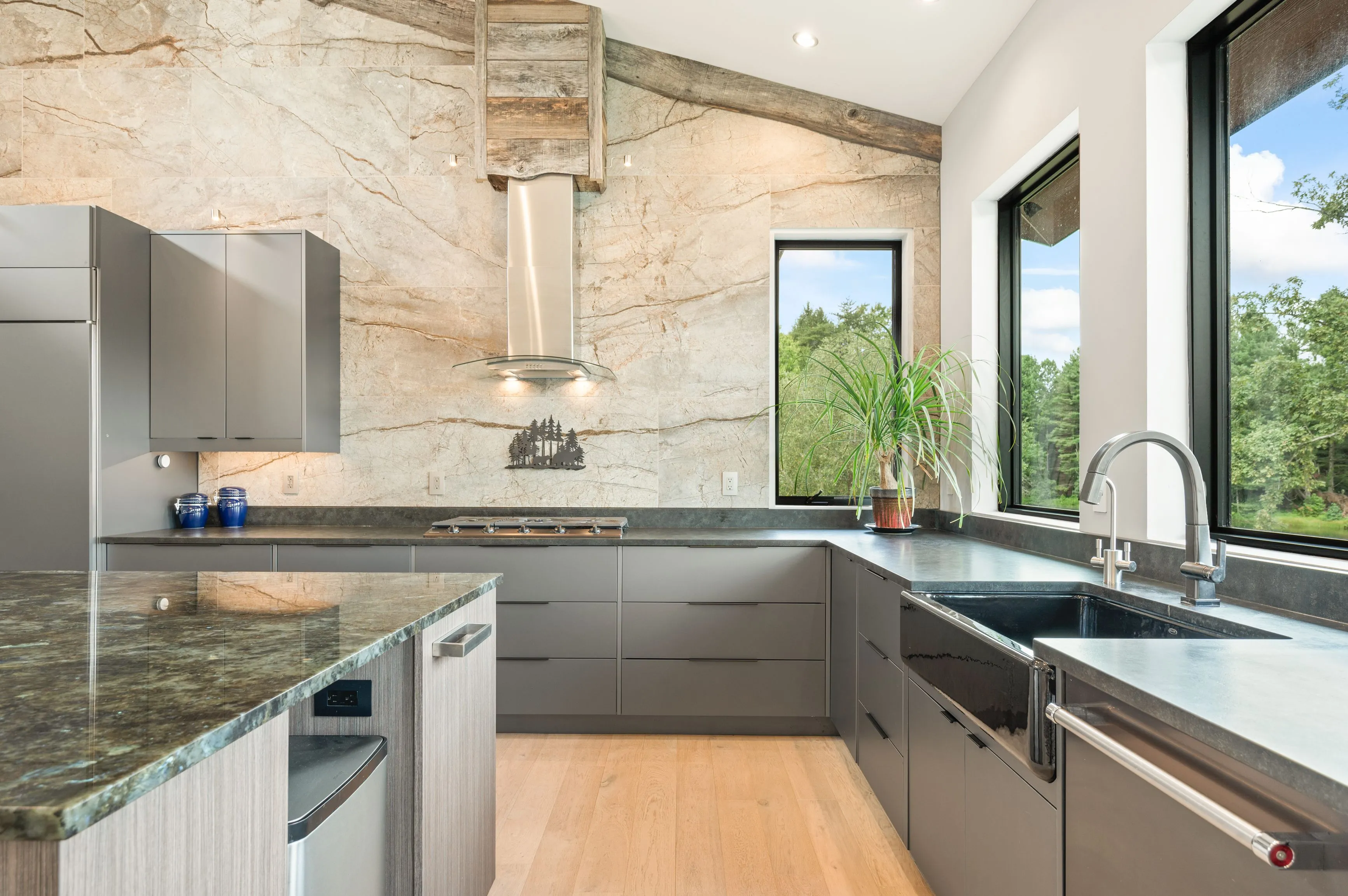 Modern kitchen interior with granite countertops, stainless steel appliances, and large windows overlooking greenery.