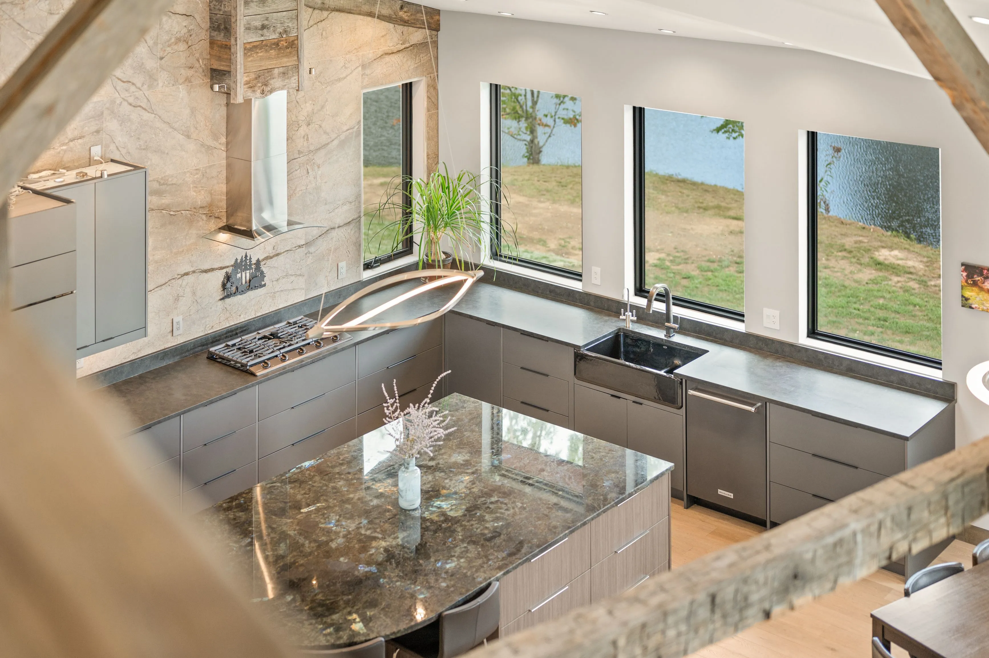 Modern kitchen interior with marble countertops, stainless steel appliances, and large windows overlooking nature.