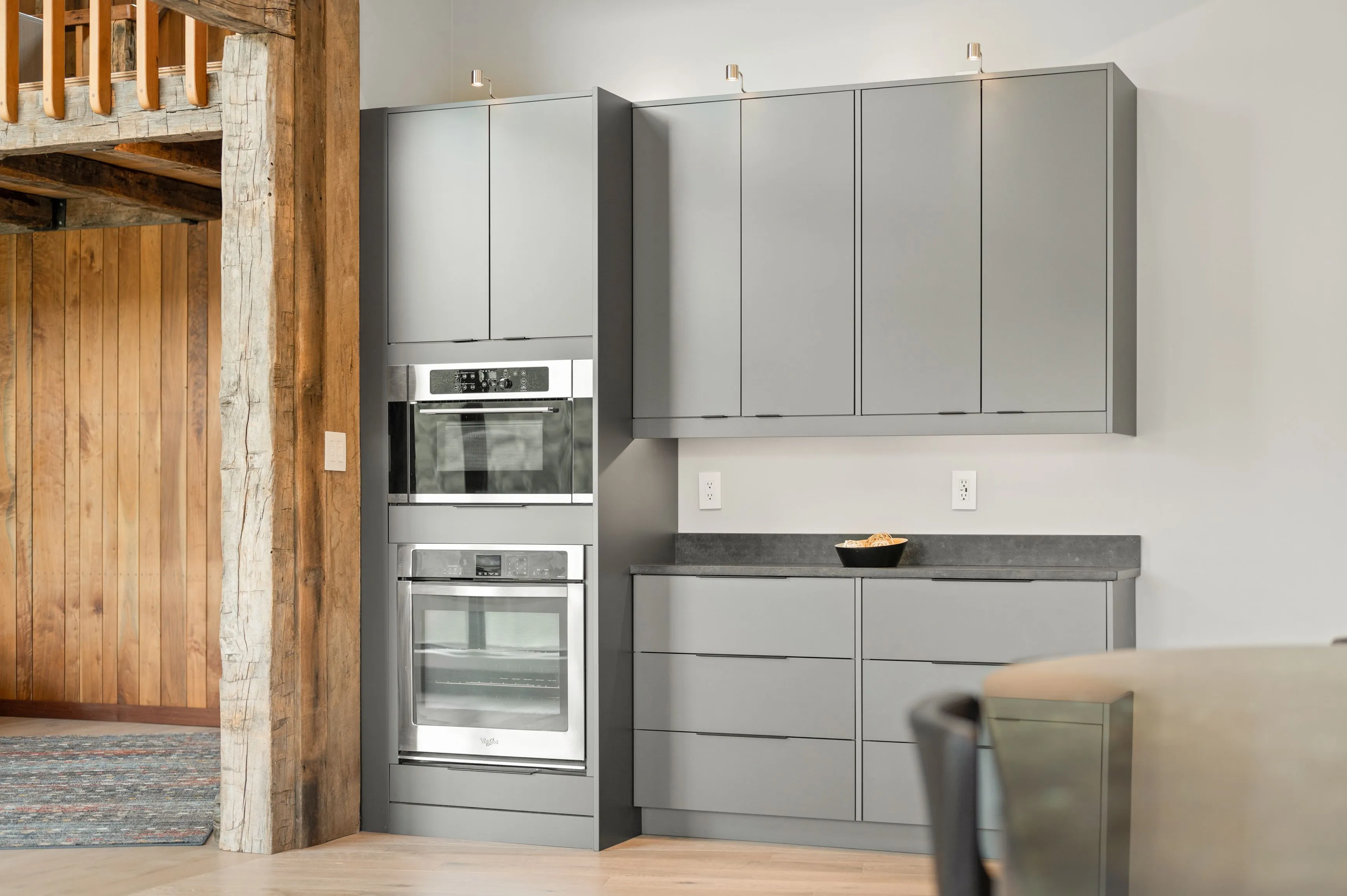Modern kitchen interior with gray cabinets, built-in stainless steel ovens, and a rustic wooden post on the left.