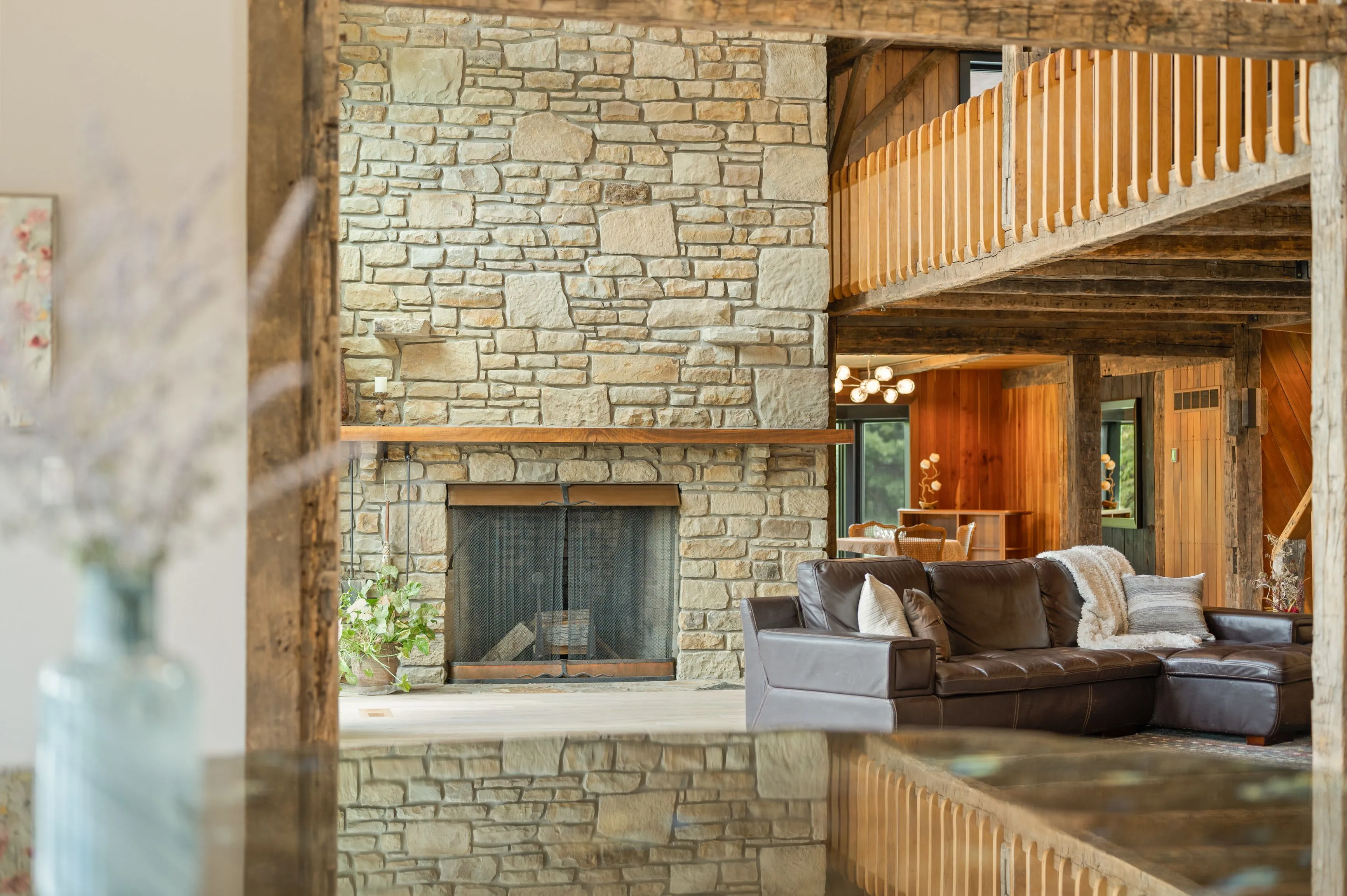 Rustic living room interior with stone fireplace, wooden beams, and leather sofa set.