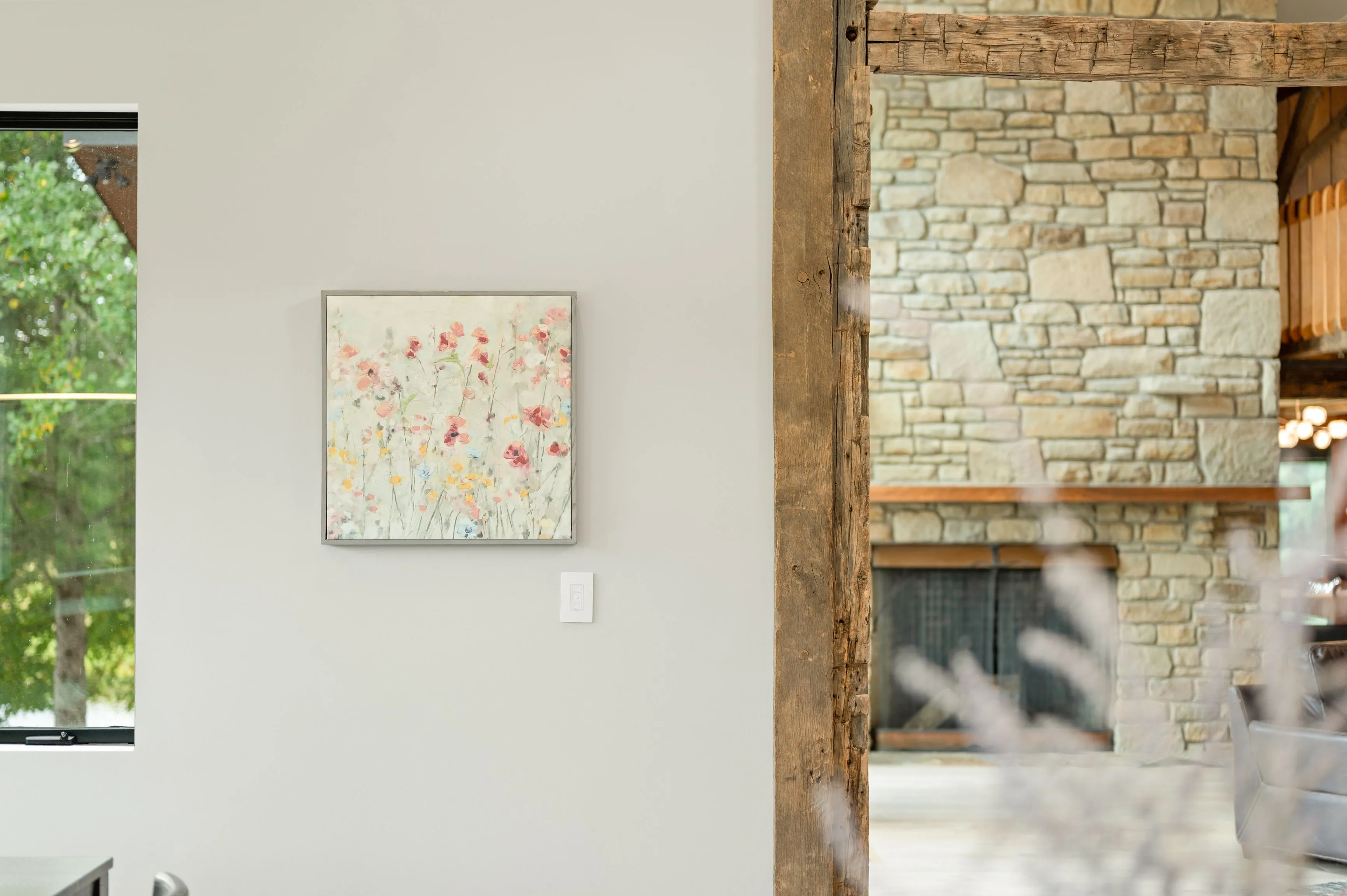 A split image showing the interior of a modern home with an abstract floral painting on the left and a rustic stone fireplace on the right, separated by a wooden beam.