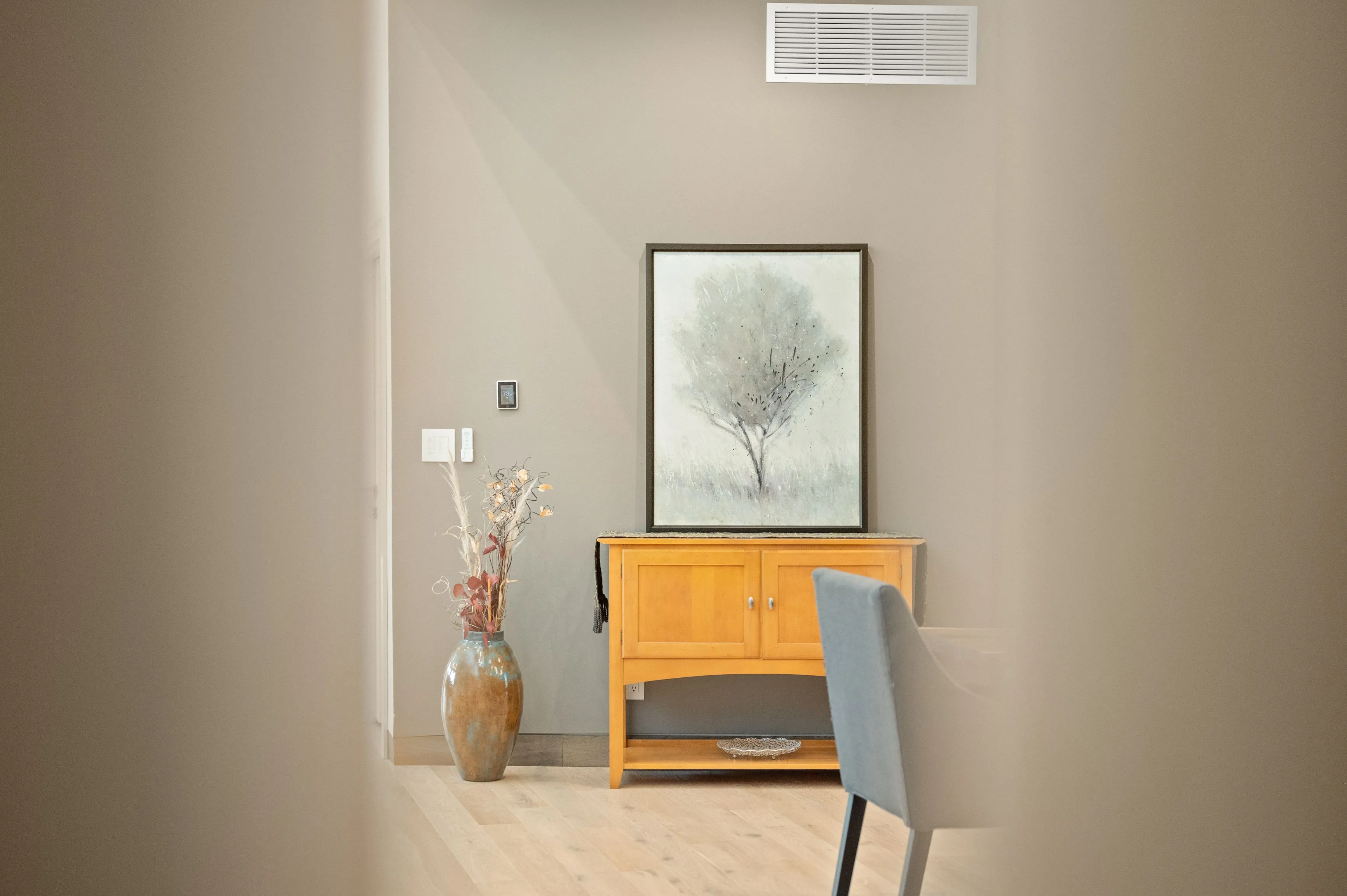 Modern interior design featuring a wooden console table with decorative vase and painting of a tree on the wall, partially viewed through an open door.