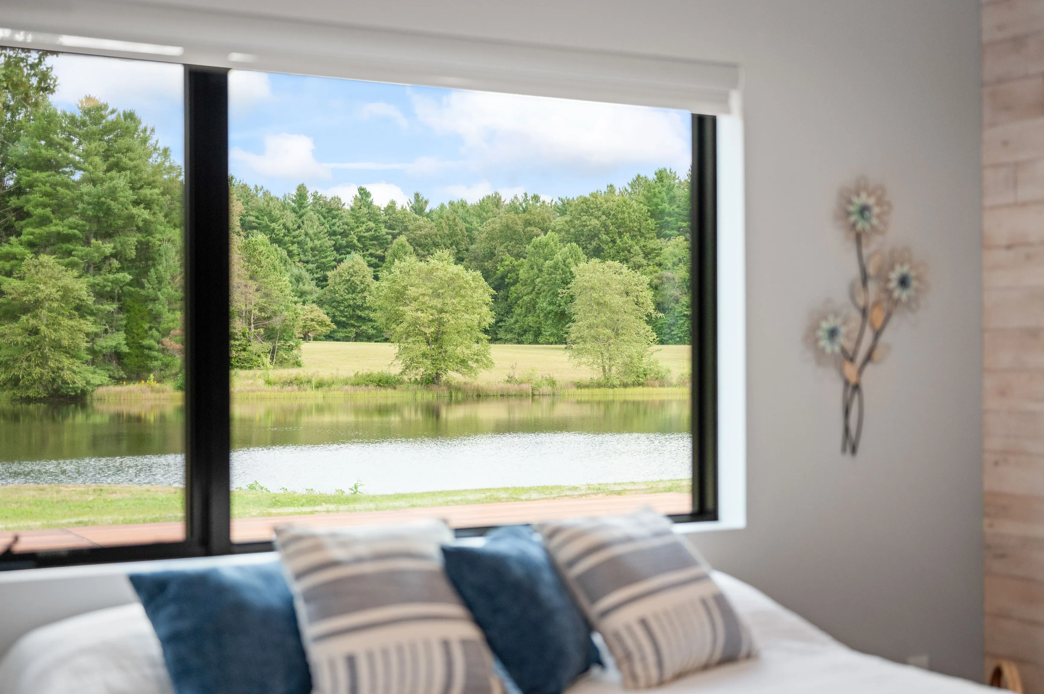 Interior view of a cozy bedroom with a large window overlooking a scenic pond surrounded by trees.
