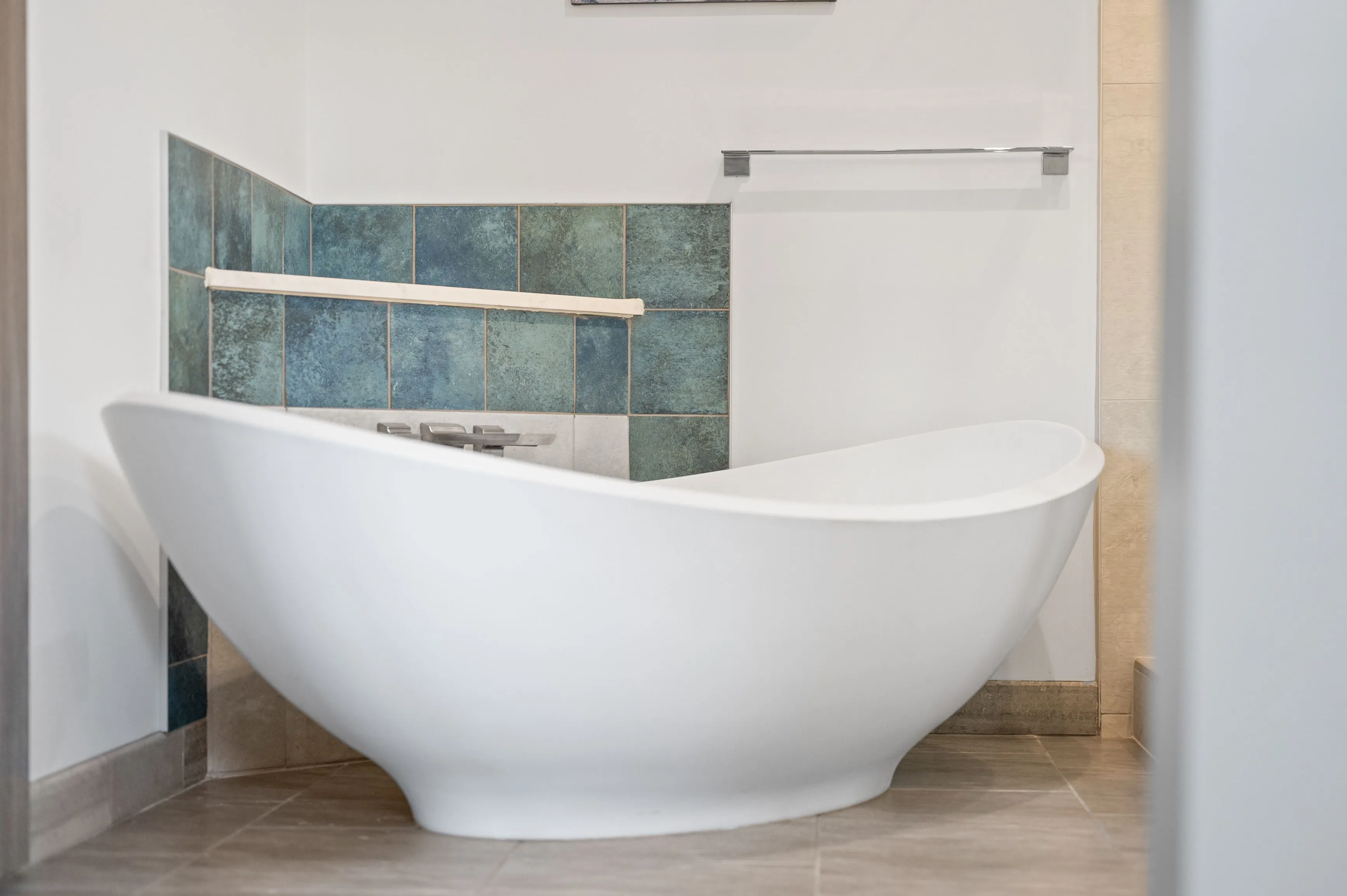 Modern free-standing bathtub in a clean bathroom with blue tile accents and tiled flooring.
