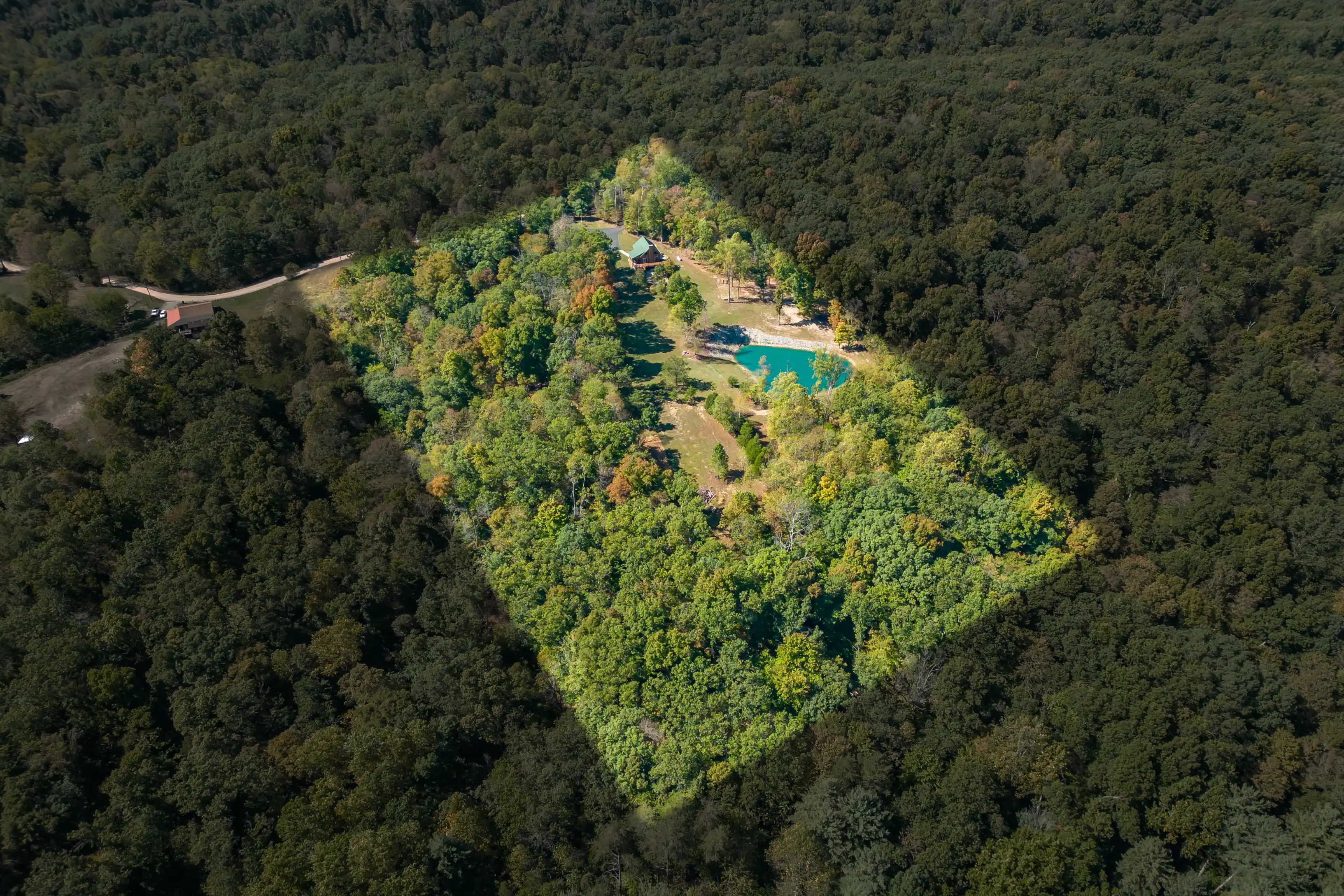 Aerial view of a forested area with a clearing containing buildings and a small pond.