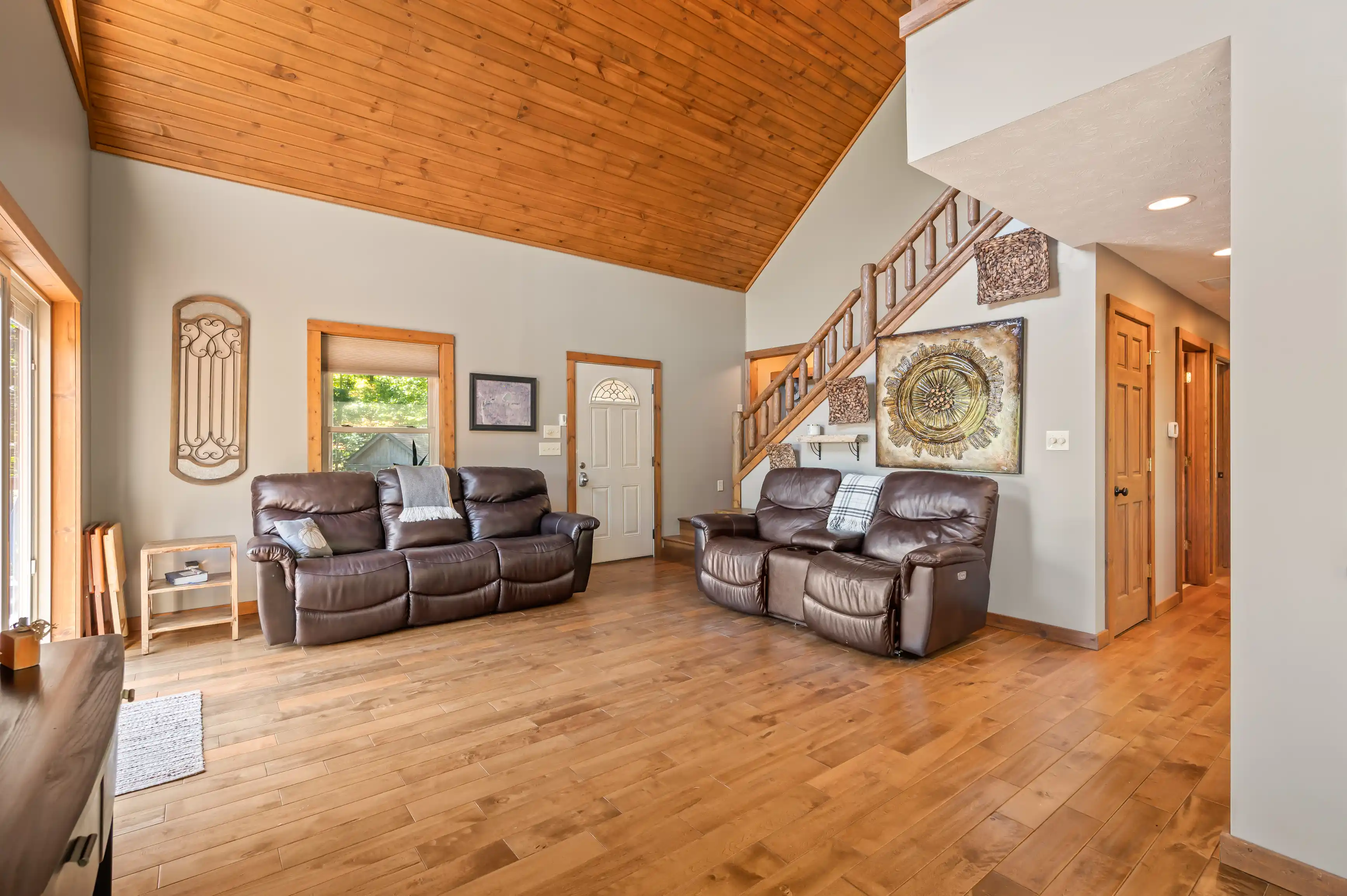 Spacious living room with vaulted wooden ceiling, leather sofas, hardwood floors, and staircase.