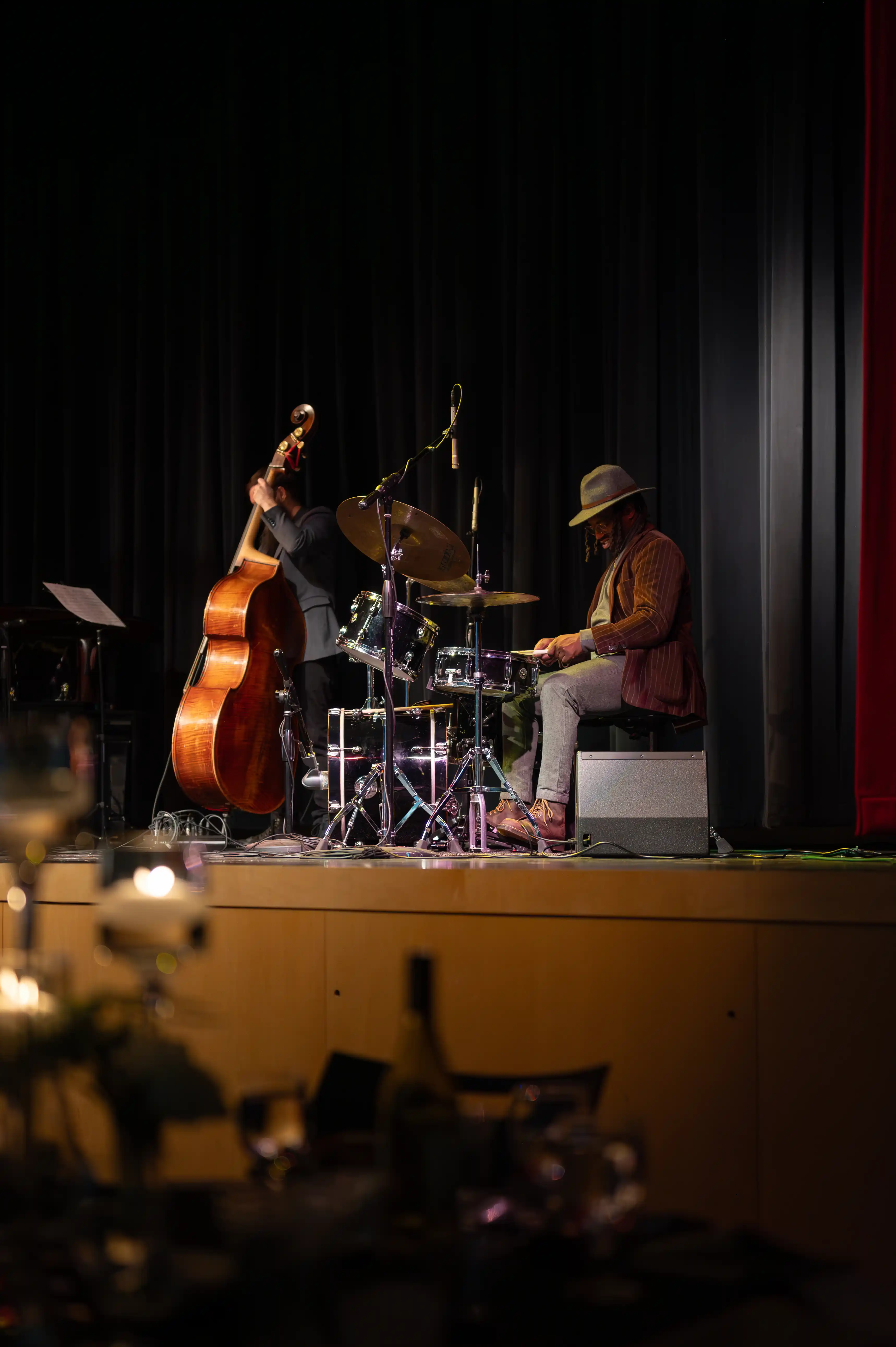 Band performing on stage with a drummer, guitarist, and a double bass player, illuminated by a spotlight.
