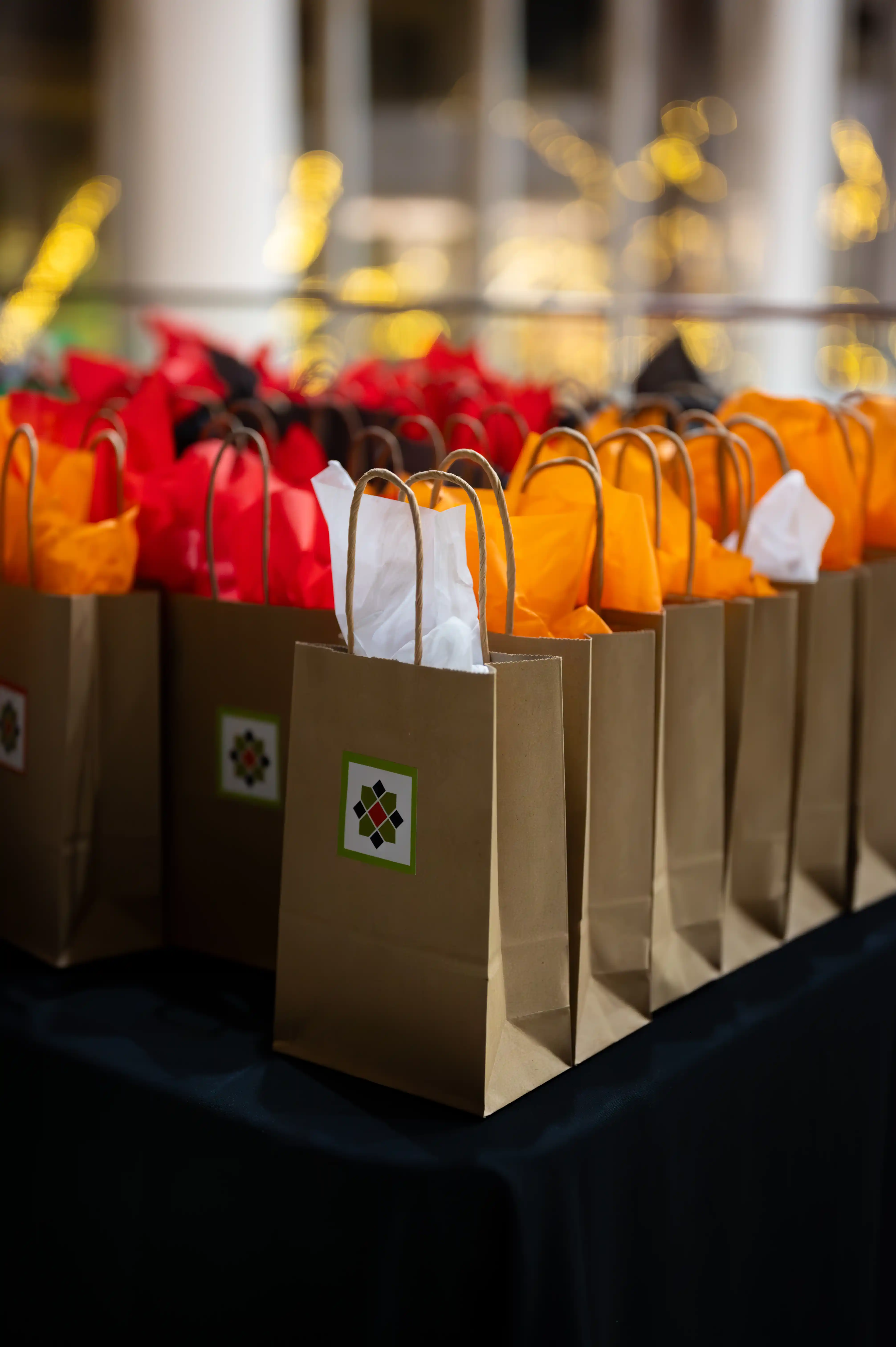 Row of colorful gift bags with tulip flower tops on a table at an event.