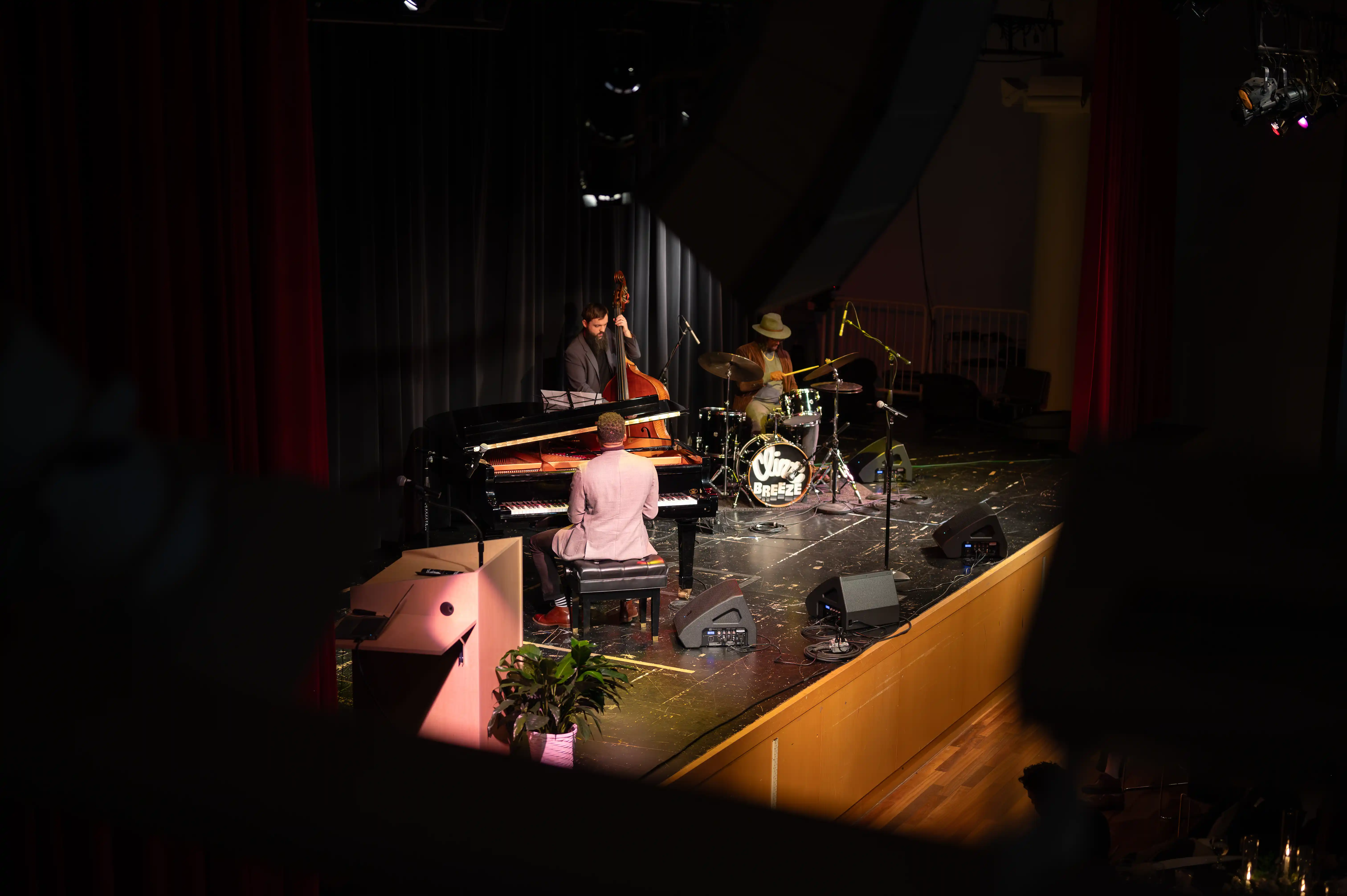 Musicians performing on stage with a piano, bass, and microphone setup in a dimly lit venue.