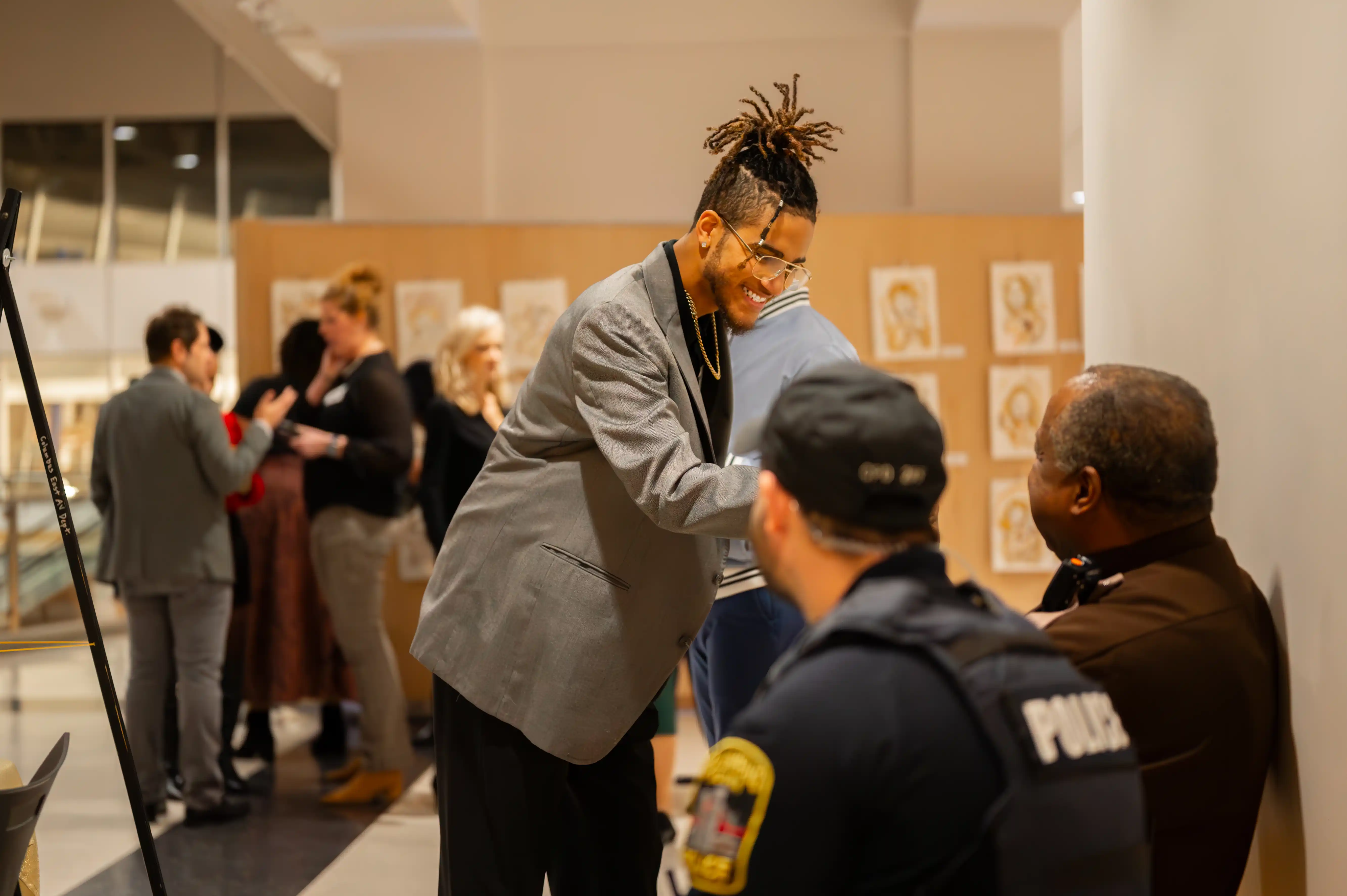 Guest at an art exhibition shaking hands with a security officer, with other attendees in the background.