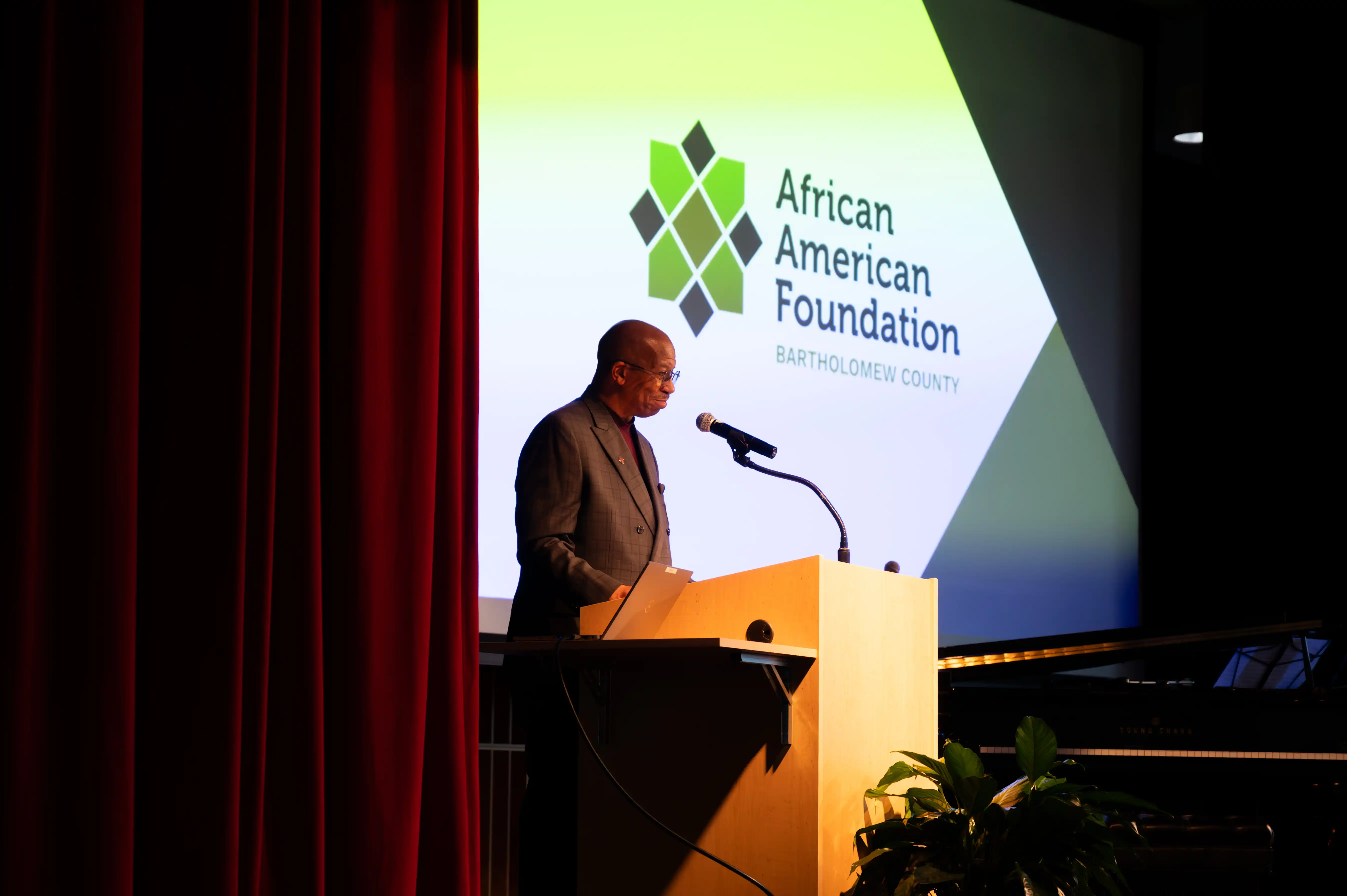 Person speaking at a podium with the African American Foundation logo projected on a screen in the background.