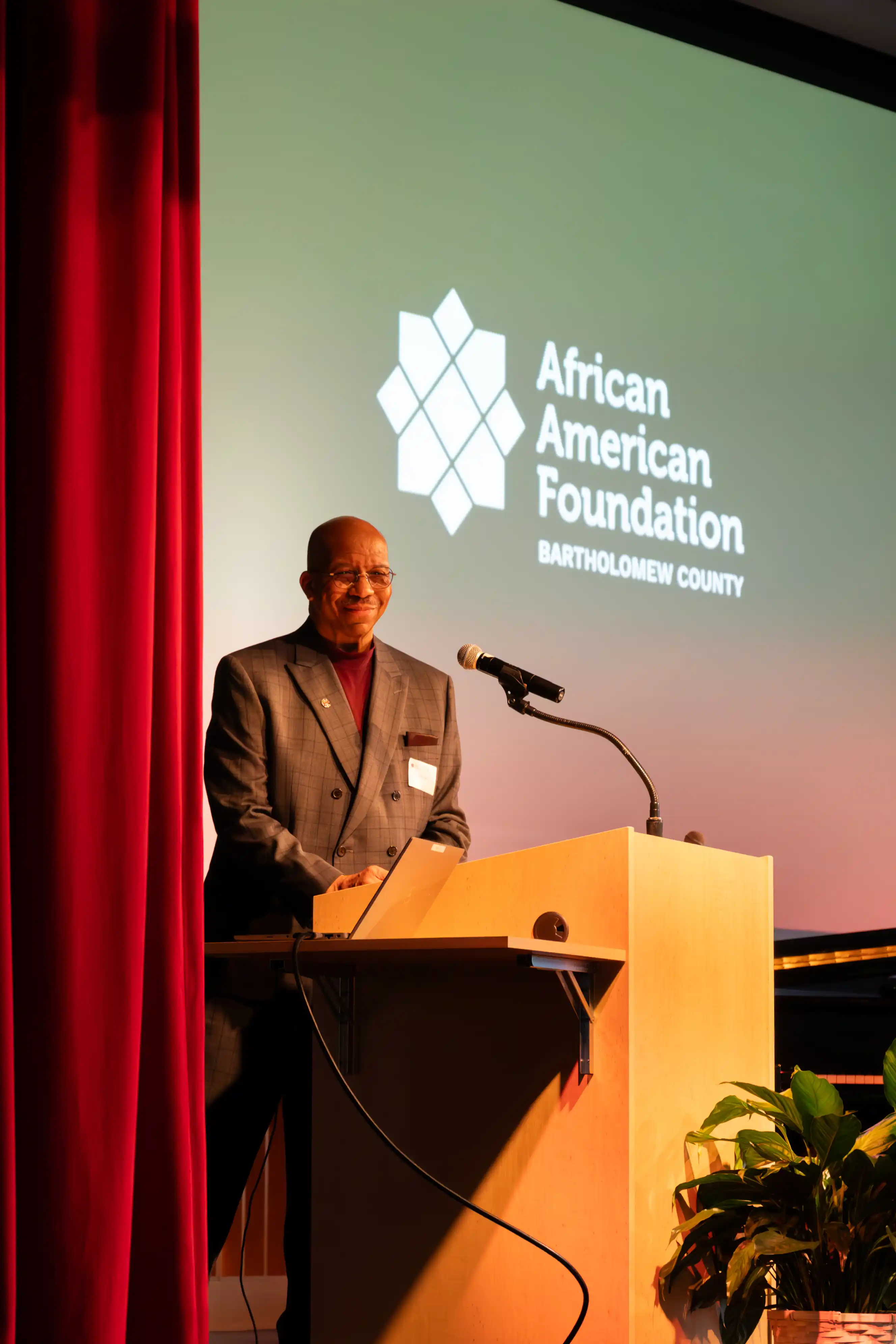 Person delivering a speech at a podium with a banner reading "African American Awareness Association" in the background.