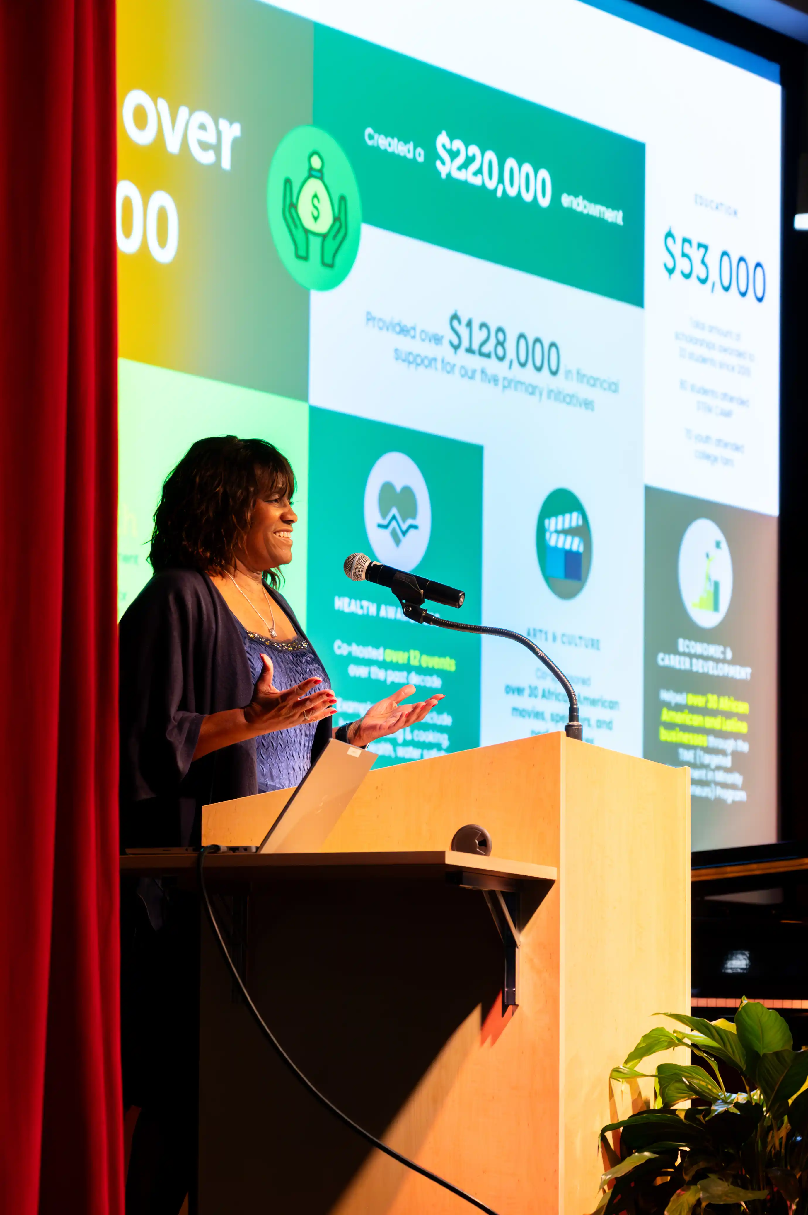 Woman presenting at a conference with a projector screen displaying financial figures behind her.
