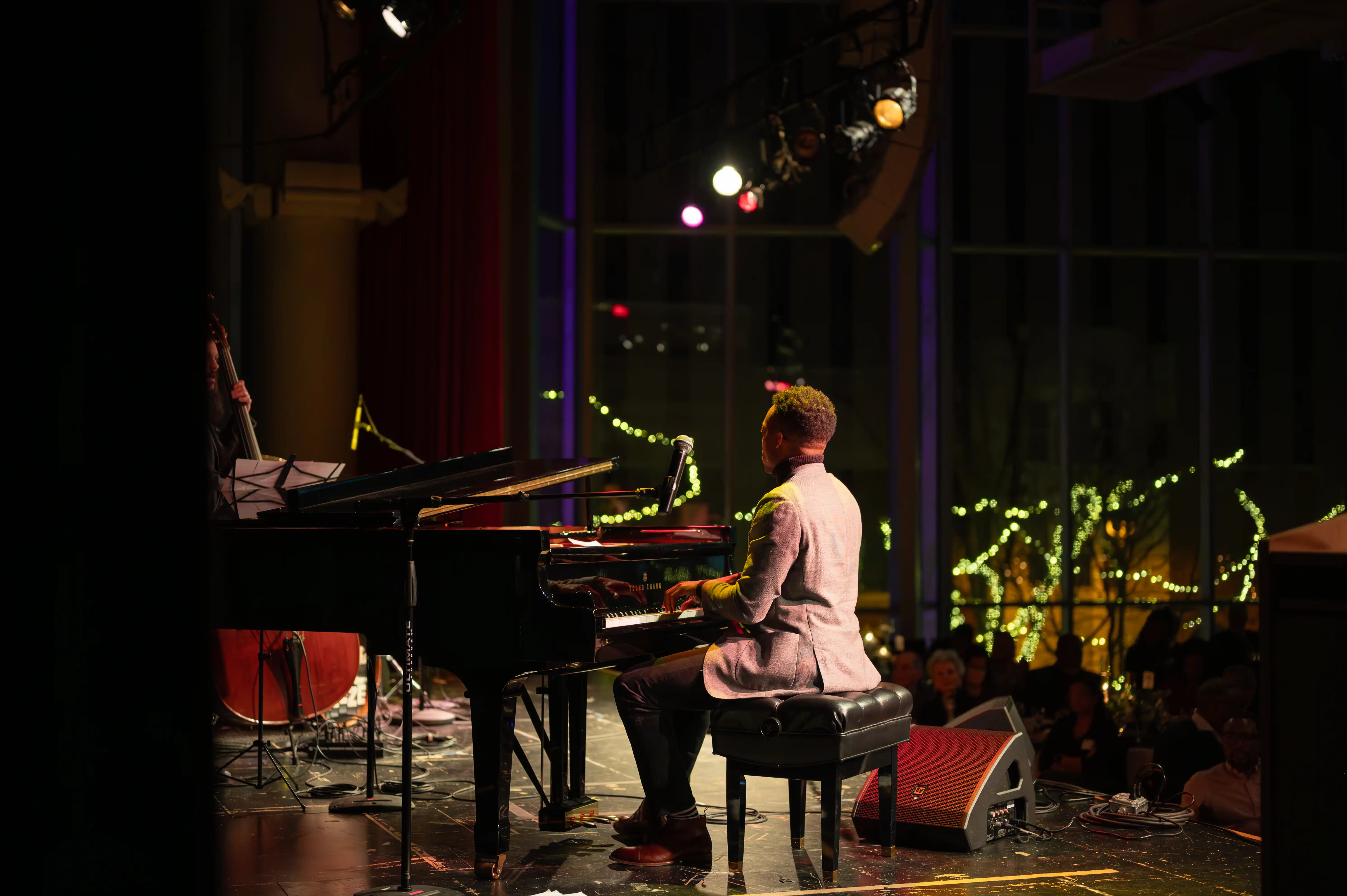 Pianist performing on stage in a dimly lit venue with a grand piano and decorative lights in the background.