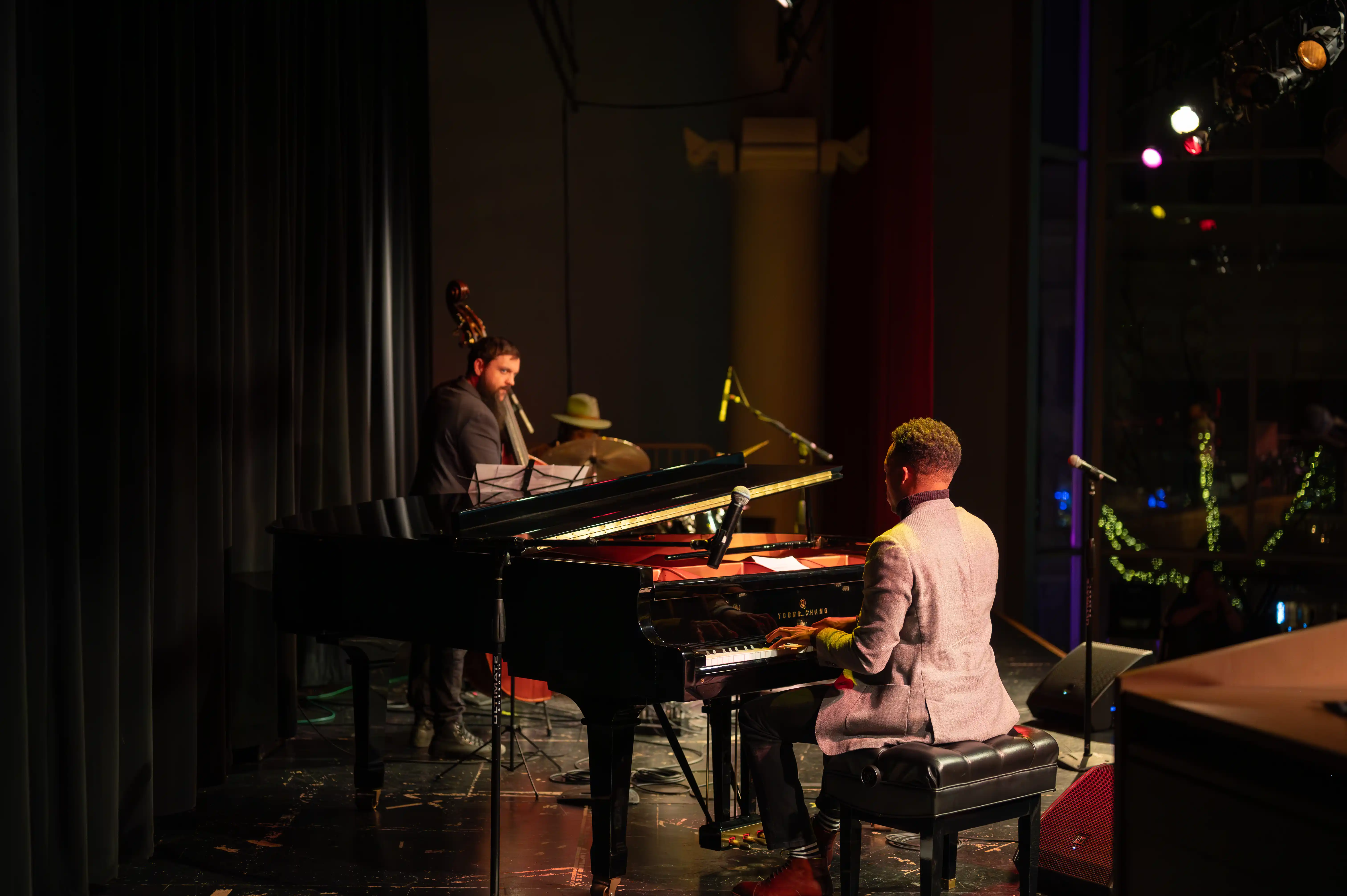 Musicians performing on stage with a pianist playing a grand piano and another musician on a keyboard.