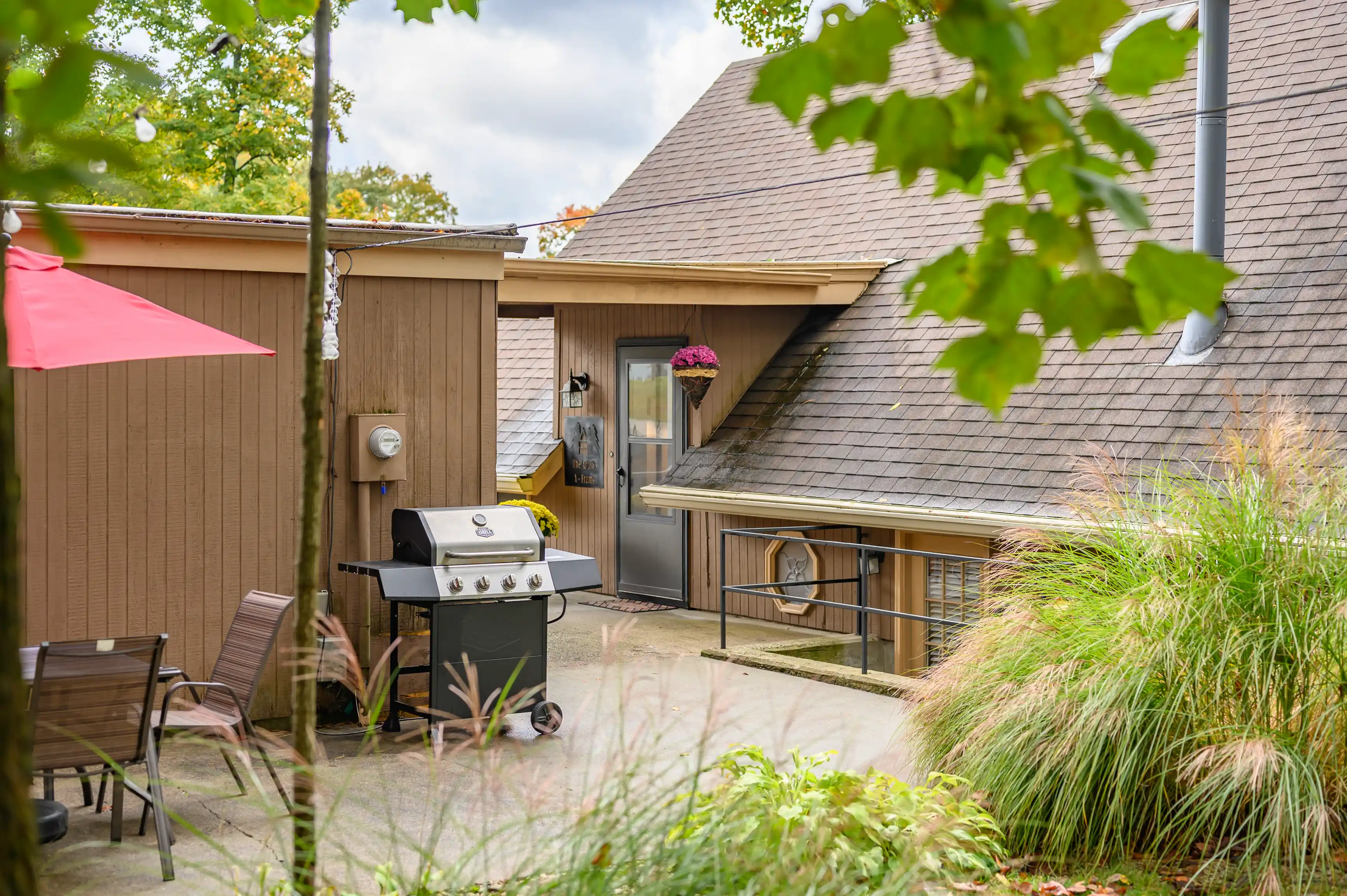 Cozy backyard patio area with a barbecue grill, outdoor furniture, and large umbrella next to a house with a person visible through the door window.