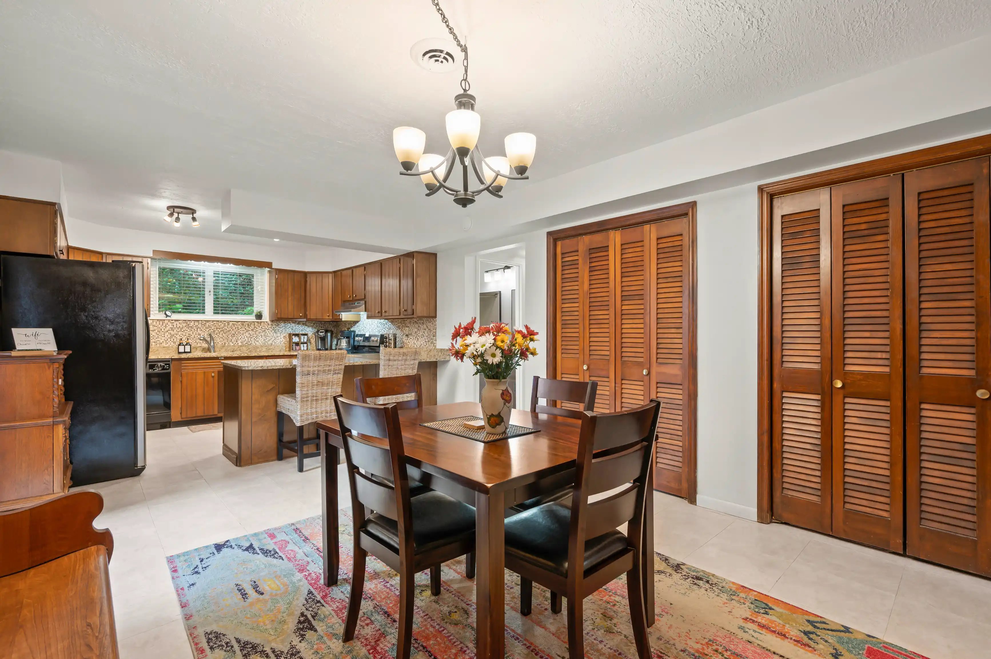 Spacious kitchen and dining area with wooden cabinetry, modern appliances, a dining table set, and a decorative rug.