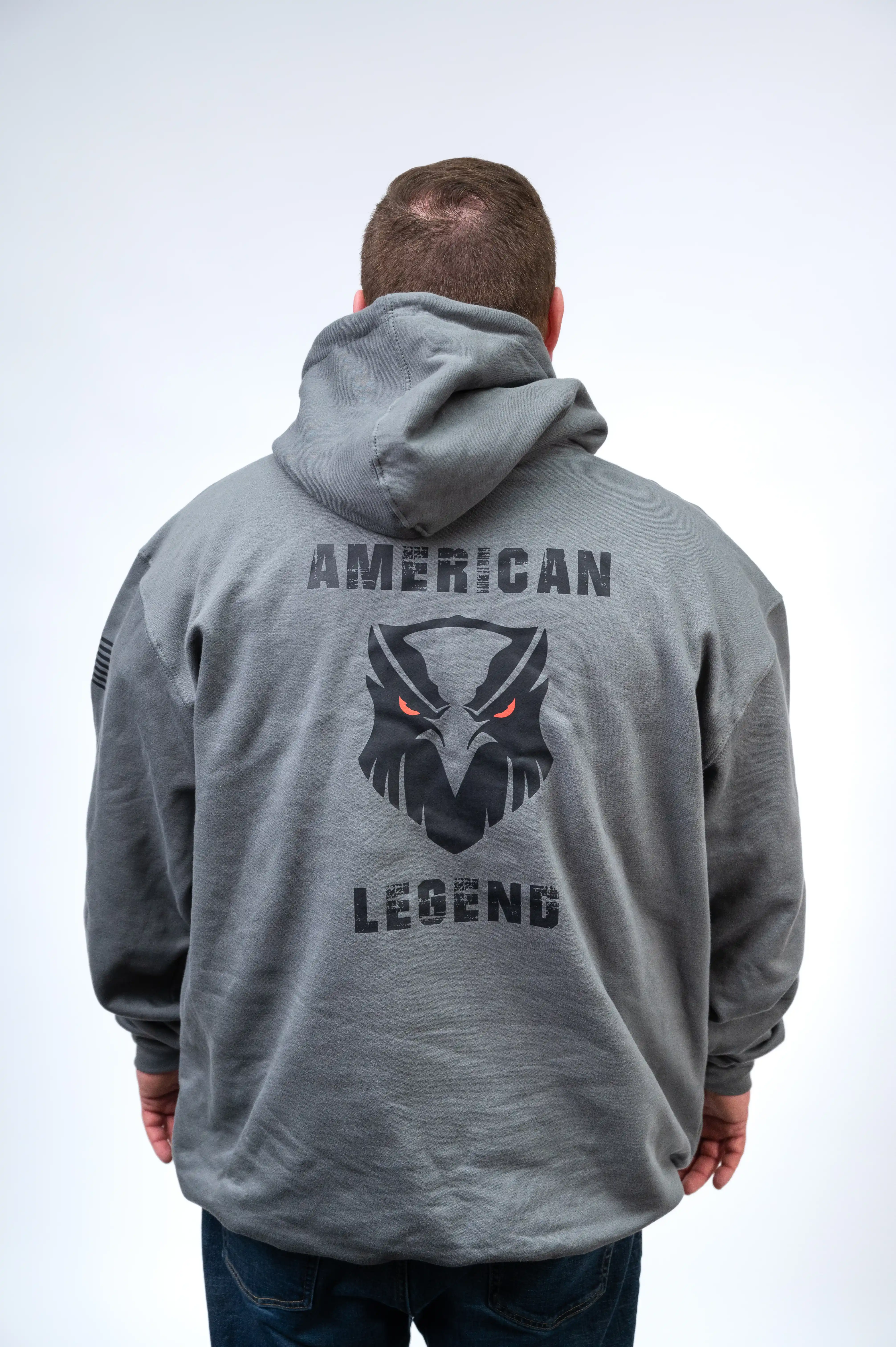 Man standing with back facing the camera, wearing a grey hooded sweatshirt with the words "AMERICAN LEGEND" and a graphic of an eagle face on it.