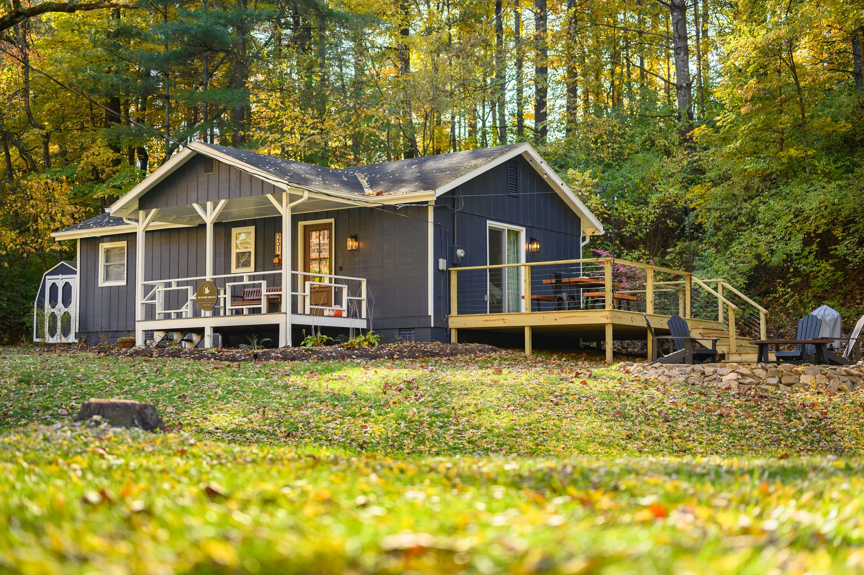 Cozy cottage house with a front porch and deck in a forest setting during autumn.