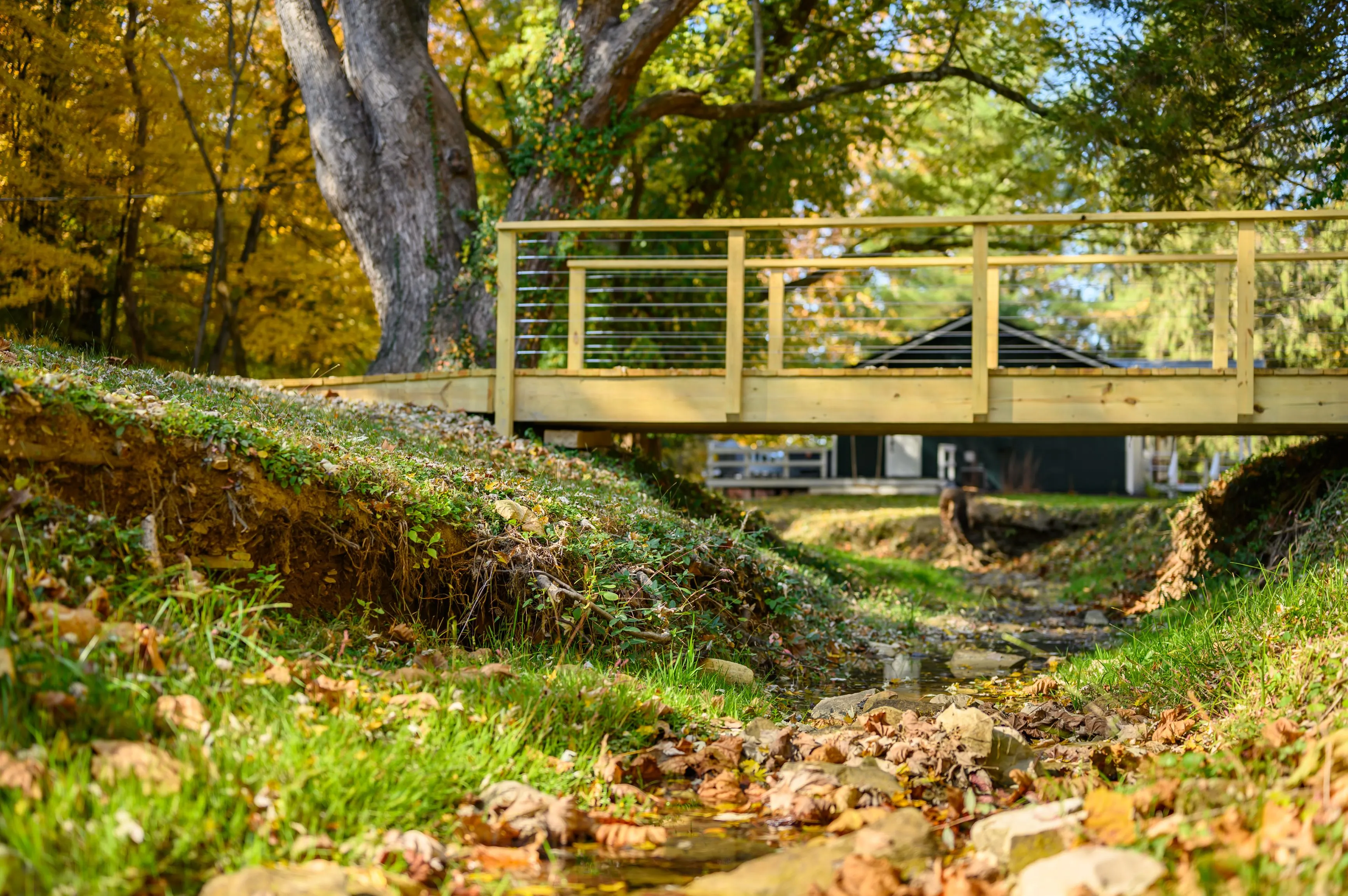 A wooden bridge over a small creek surrounded by autumn foliage in a park setting.