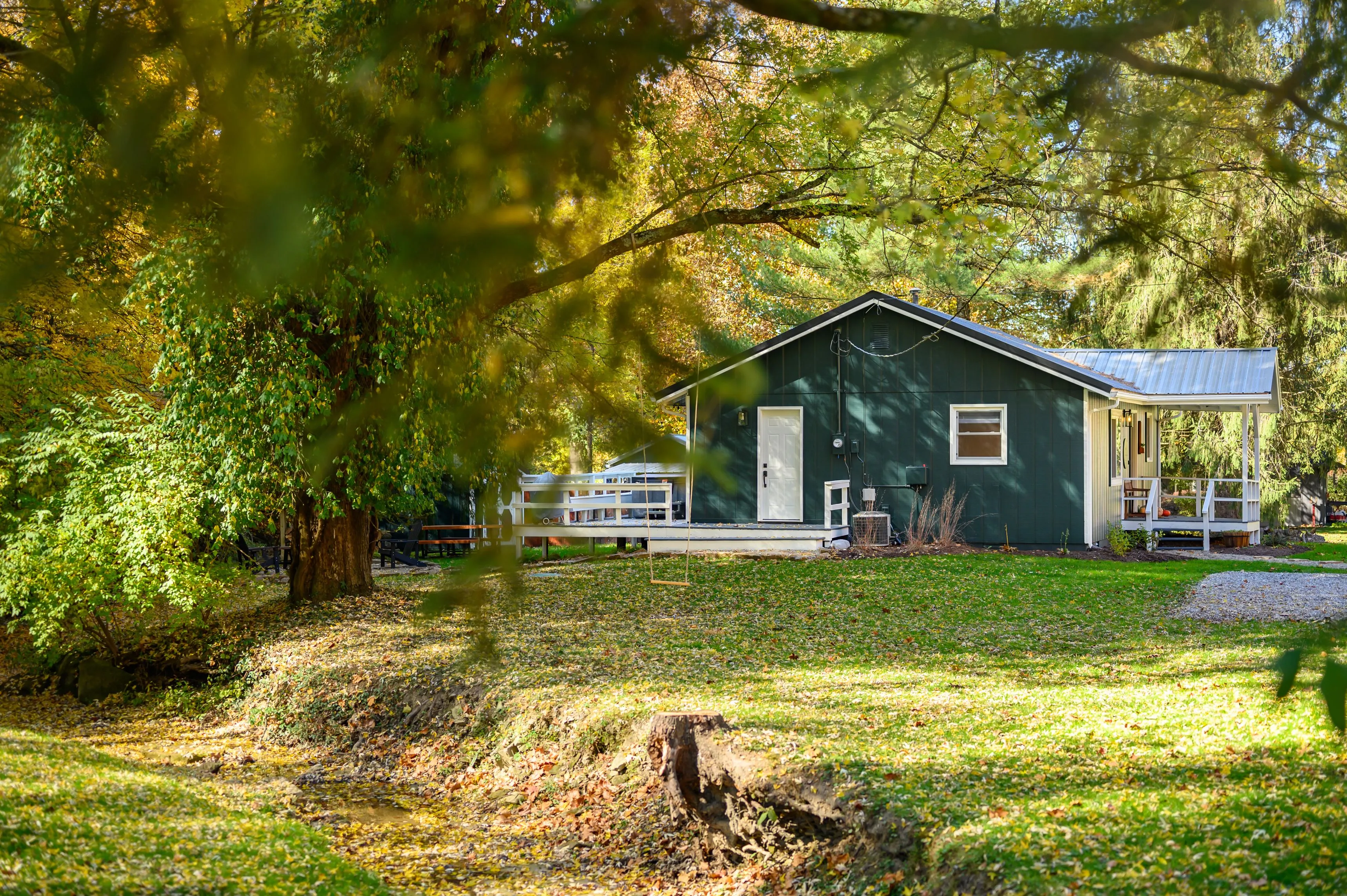 Cozy green cabin with a covered porch surrounded by autumn foliage in a serene wooded area.