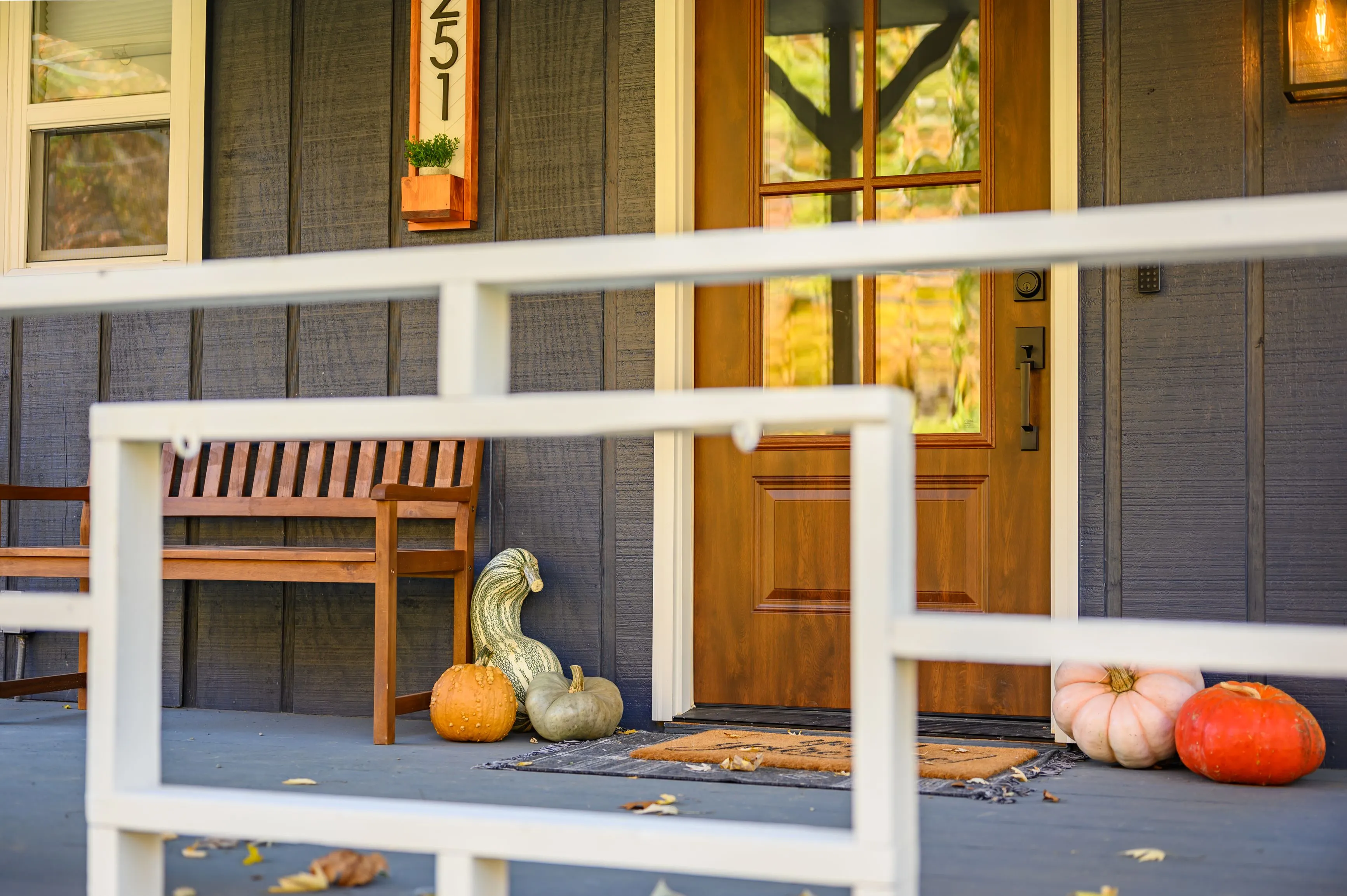 A cozy front porch with a wooden bench and an assortment of pumpkins near the front door of a house with autumn decorations.