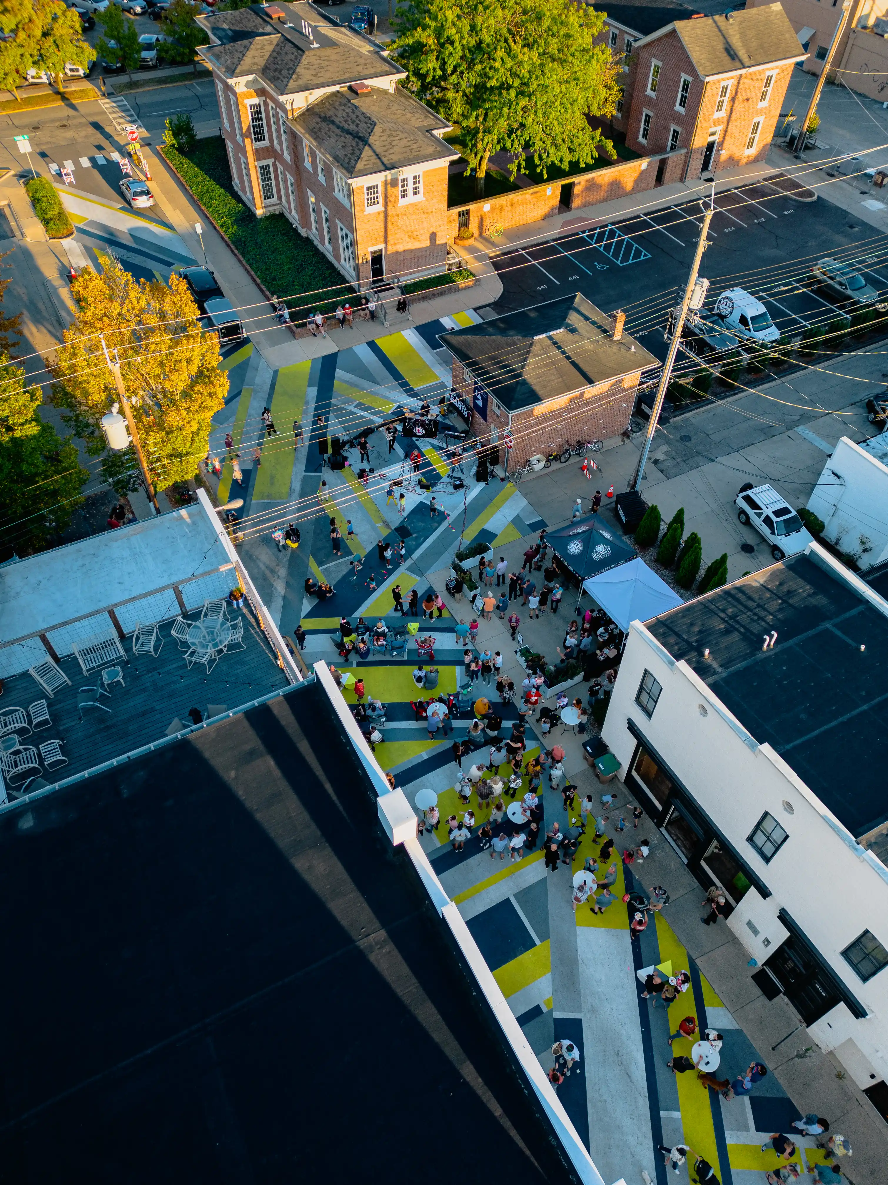 Aerial view of a bustling street with pedestrians, vehicles, and surrounding buildings in an urban environment at dusk.
