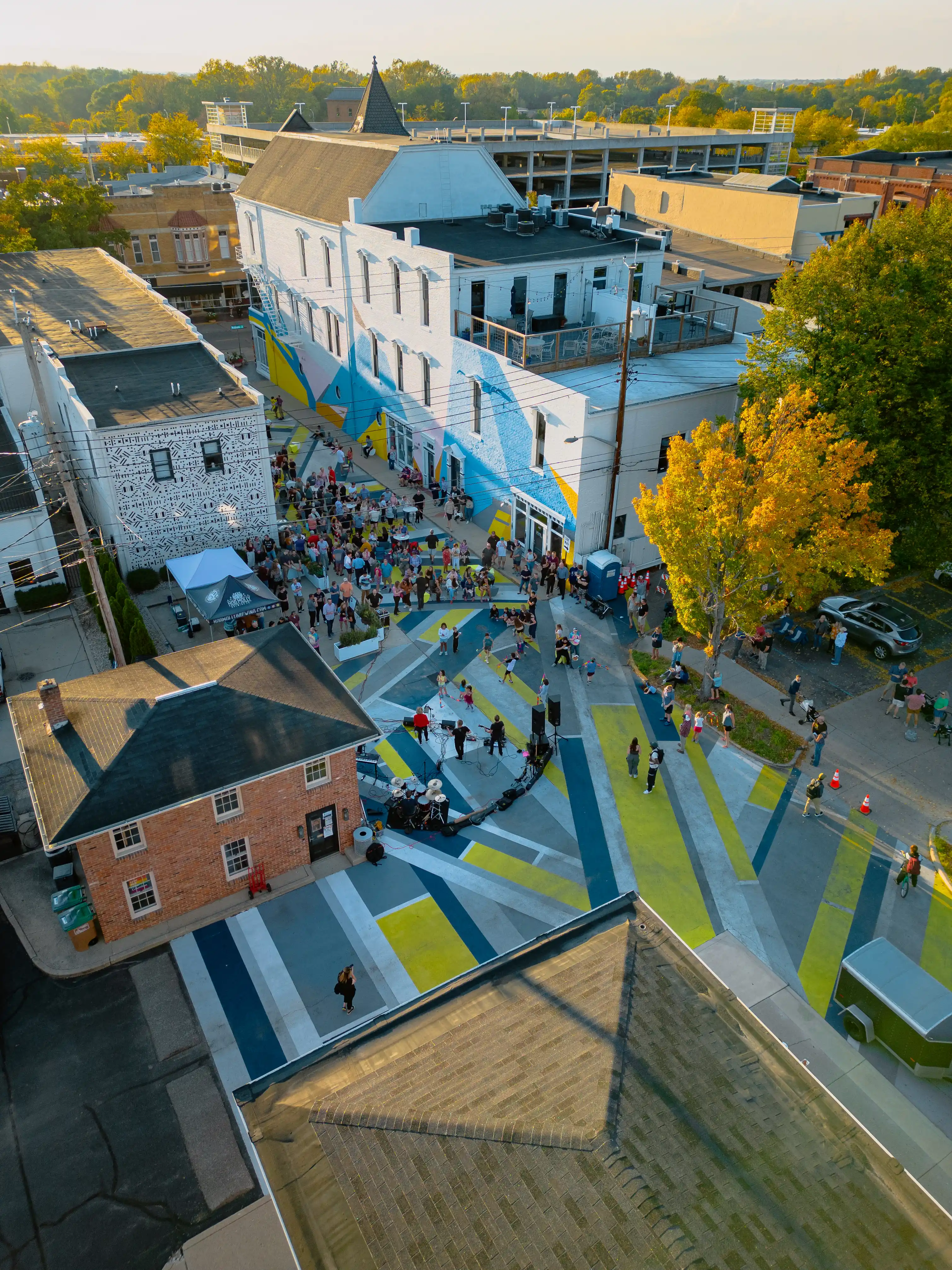 Aerial view of an outdoor street art installation with geometric patterns on pavements and walls in an urban setting, with people interacting with the space.
