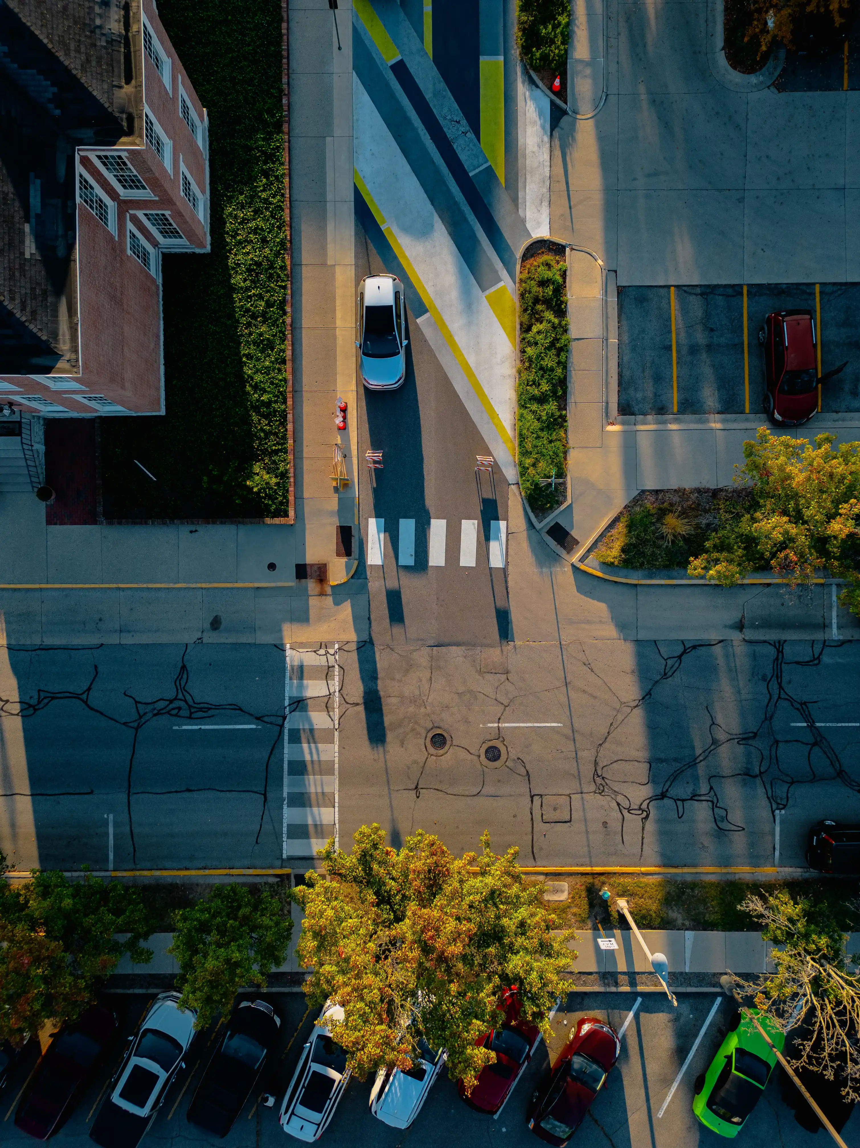 Aerial view of a street intersection with crosswalks, cars, and autumn trees.