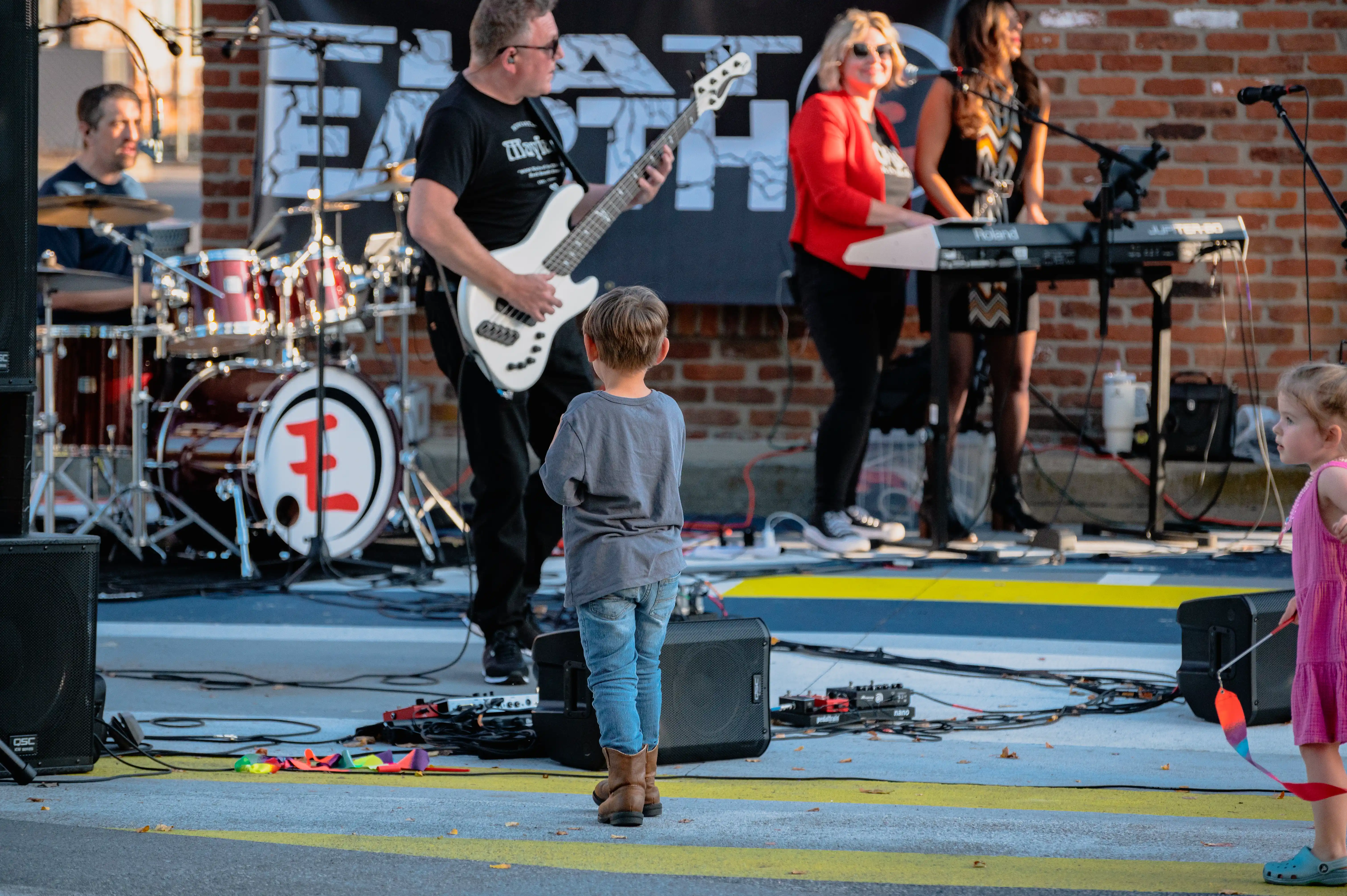 A live band performing on stage with a guitarist in the forefront and a child watching intently in the foreground.