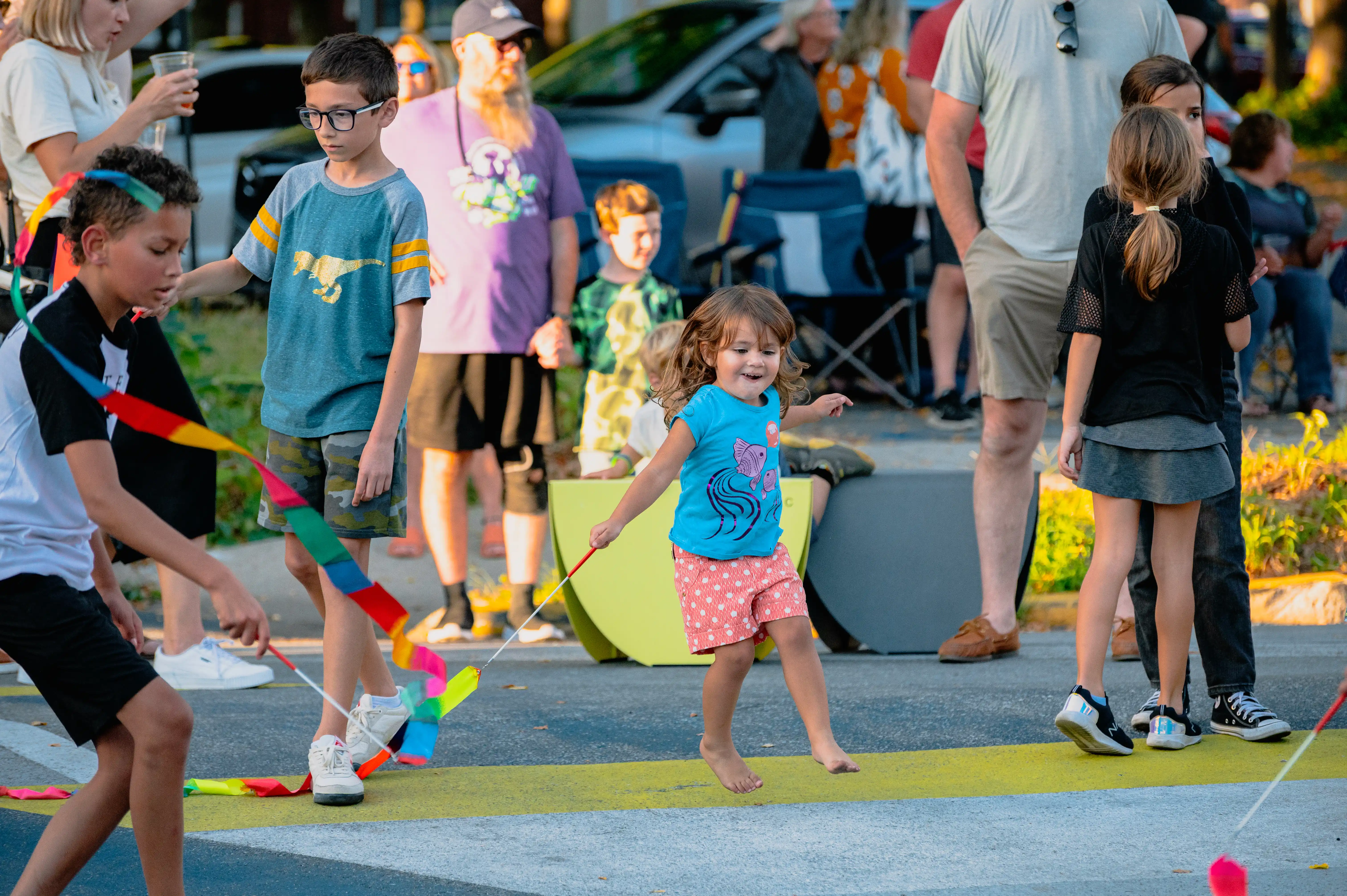 Children playing with jump ropes on a closed street during a community event while adults watch.