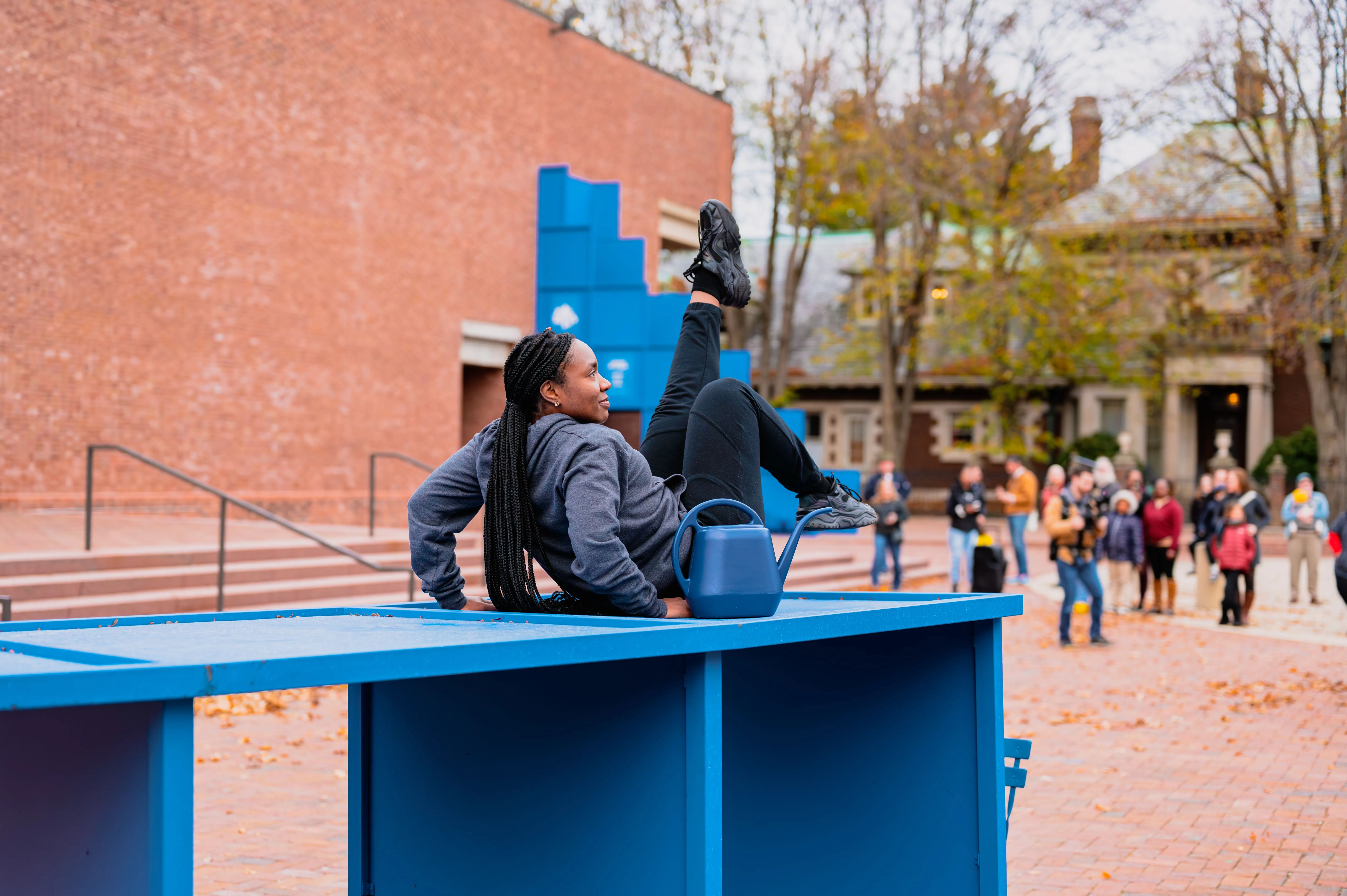 People sitting and chatting on a blue outdoor structure with other individuals walking by in the background.