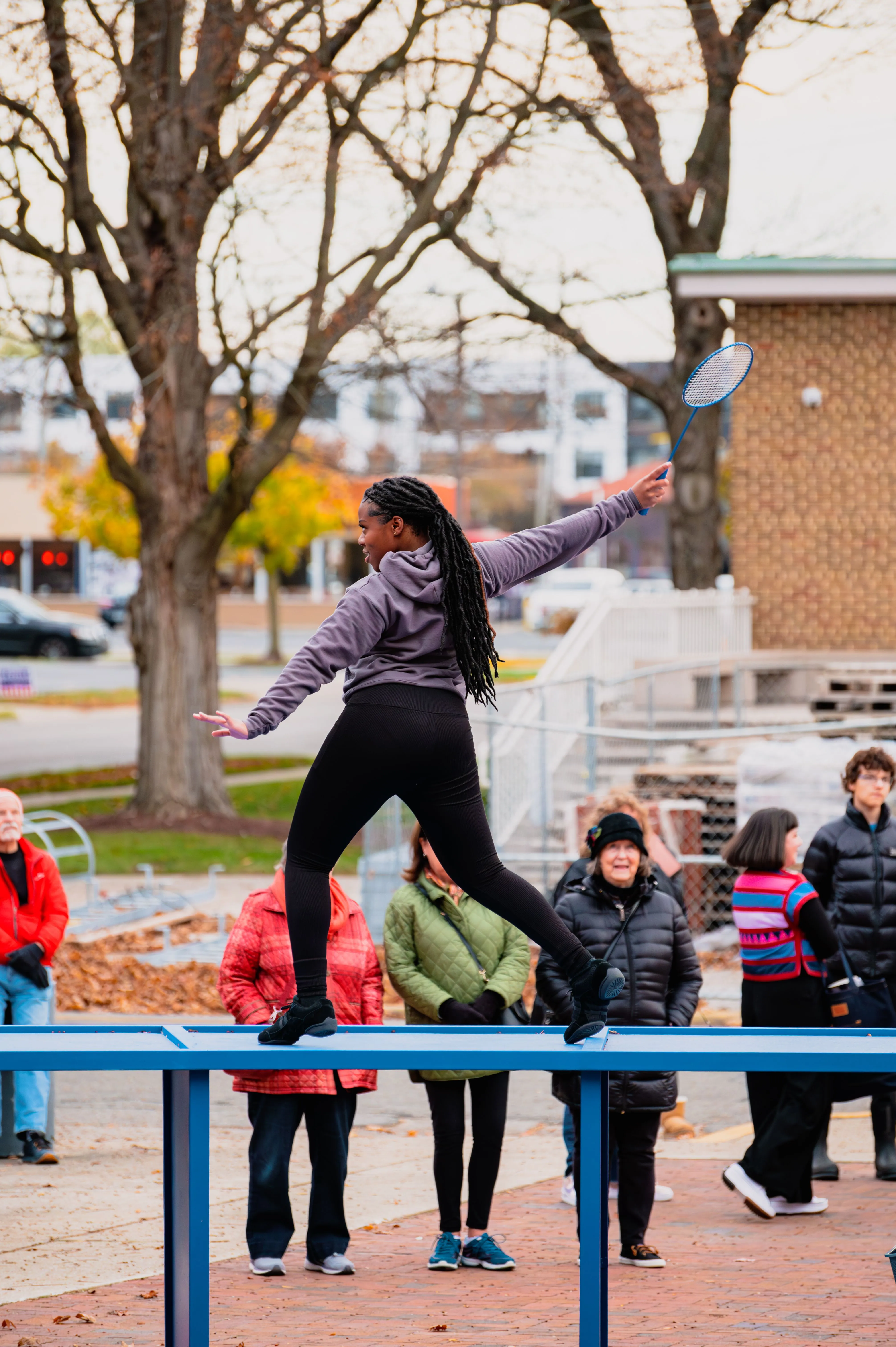 Person balancing on a metal beam in a park with onlookers in the background.