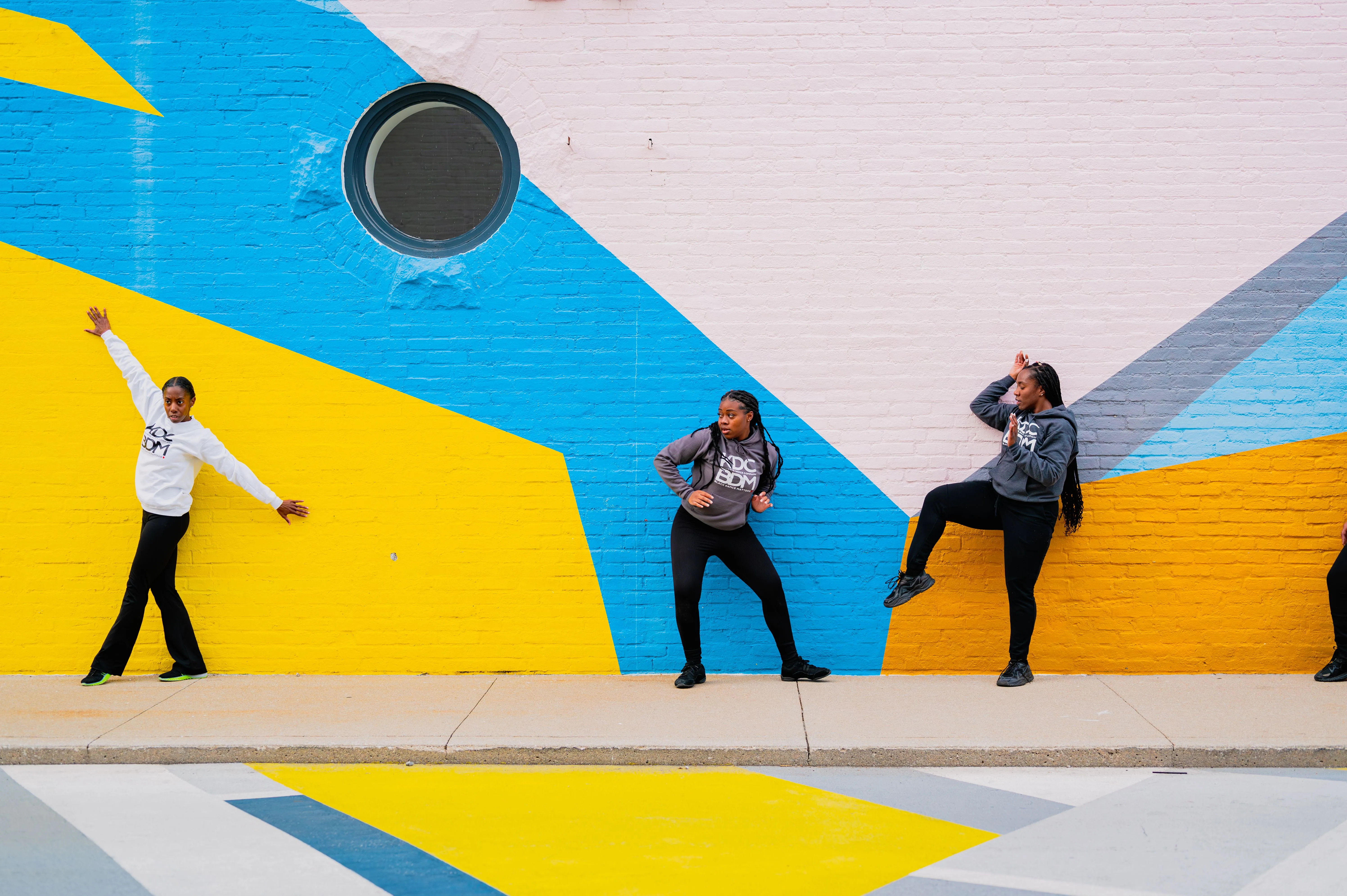 Three people posing playfully against a colorful geometric mural on a wall.