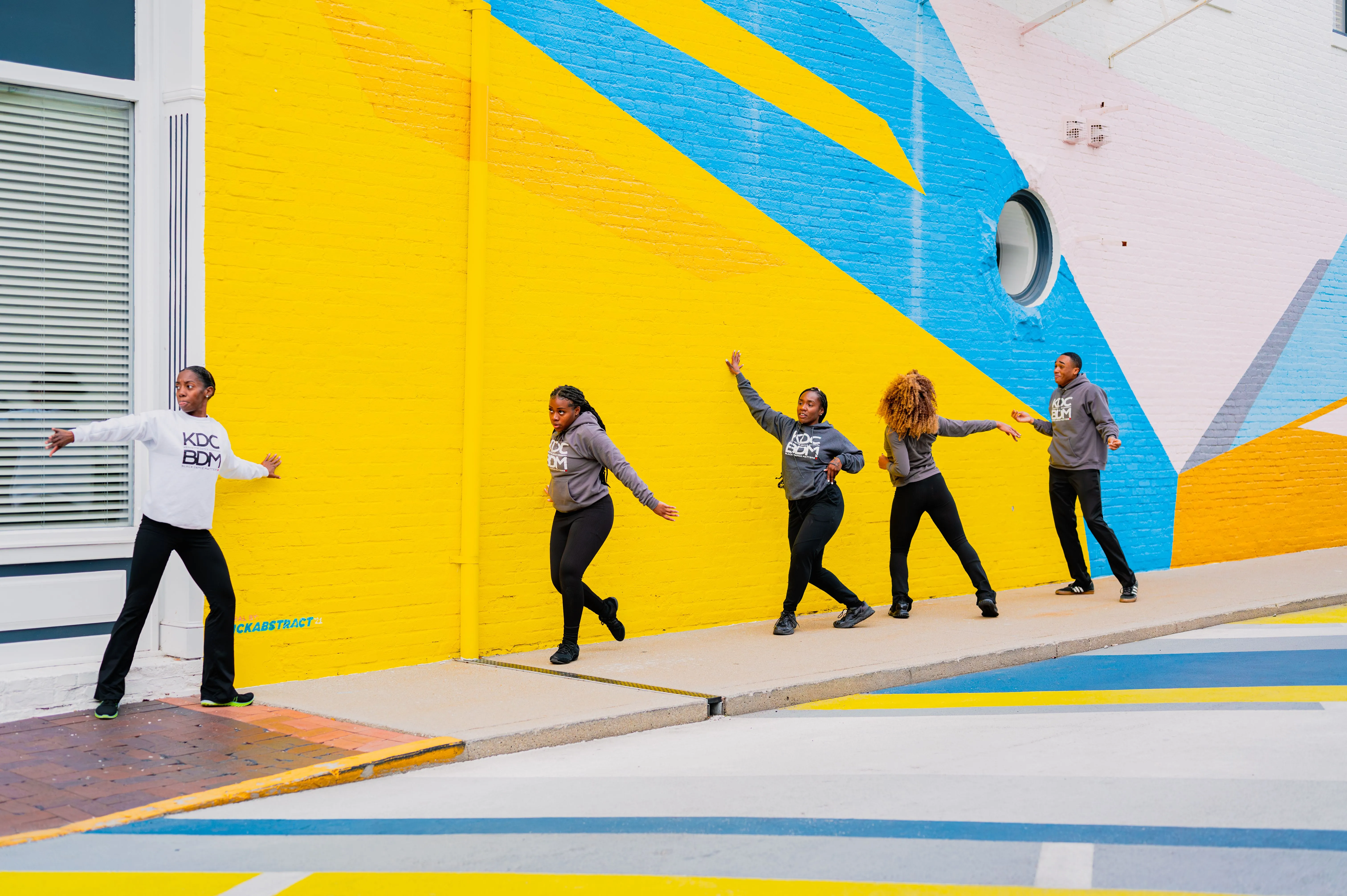 Group of people in a playful pose walking in line against a colorful geometric background.