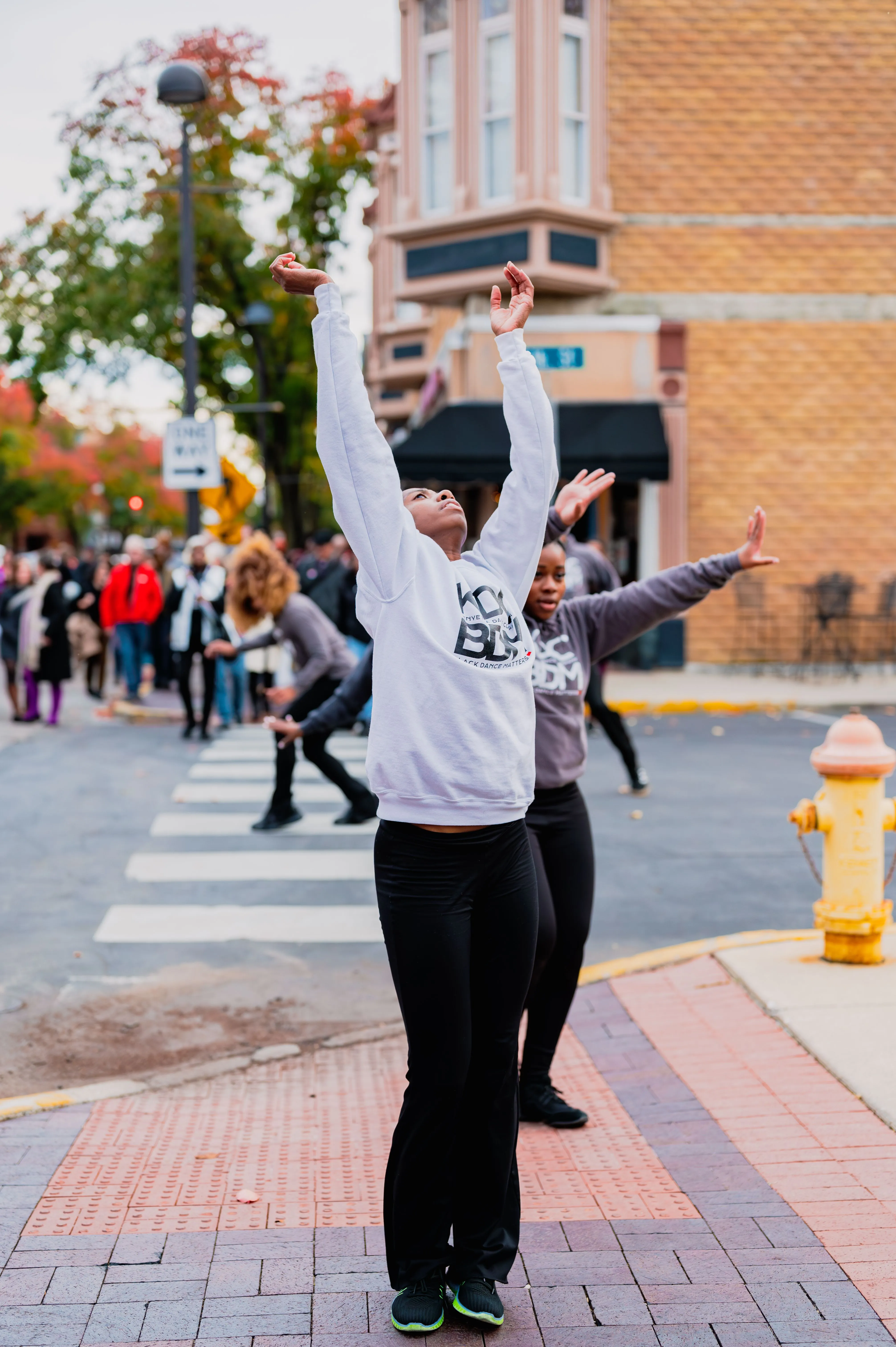 Person in excitement raising arms on a city street with other pedestrians in the background.